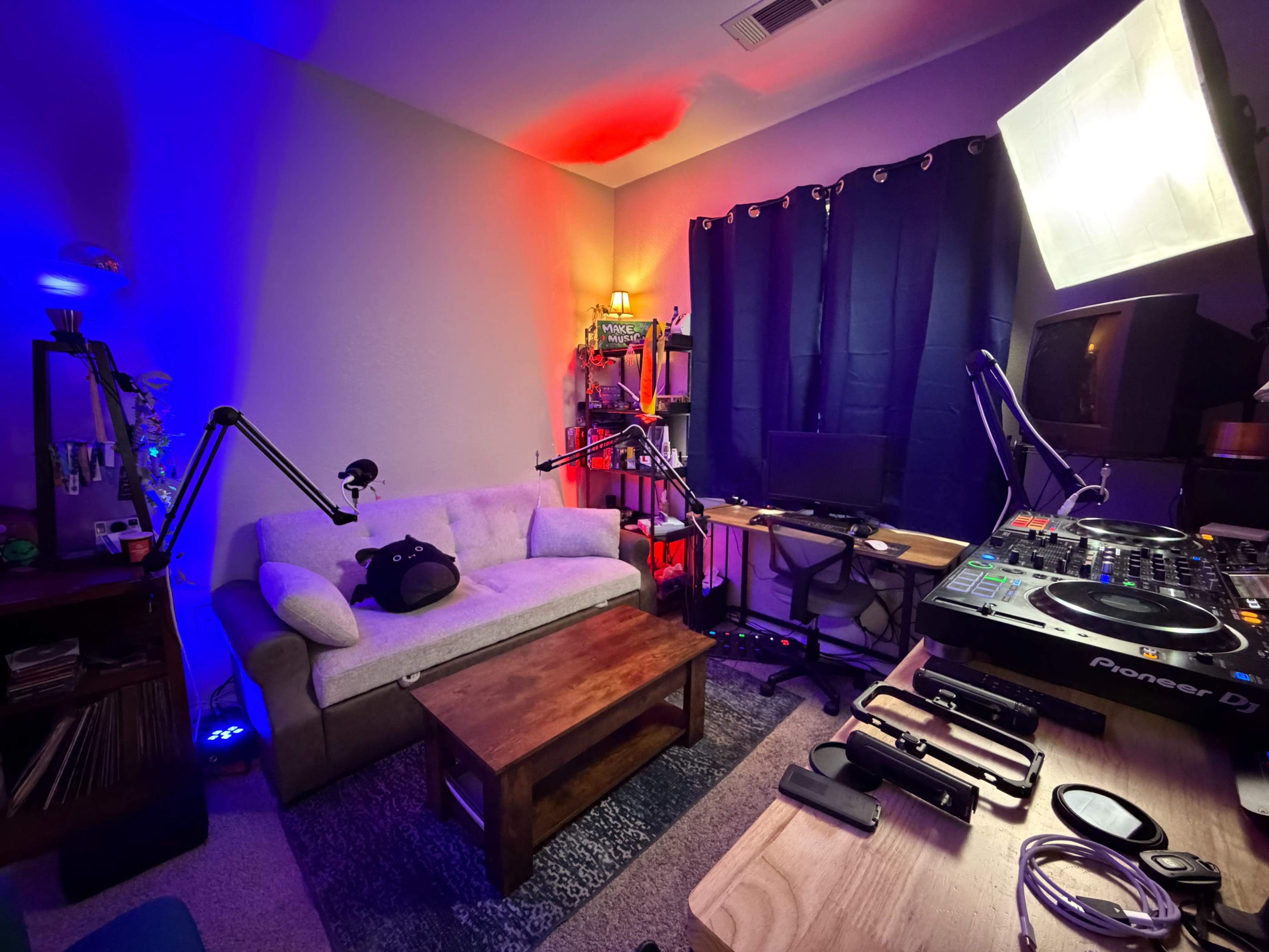The room features a cozy seating area with a gray couch and a wooden coffee table, while studio equipment is arranged beside a black curtain.