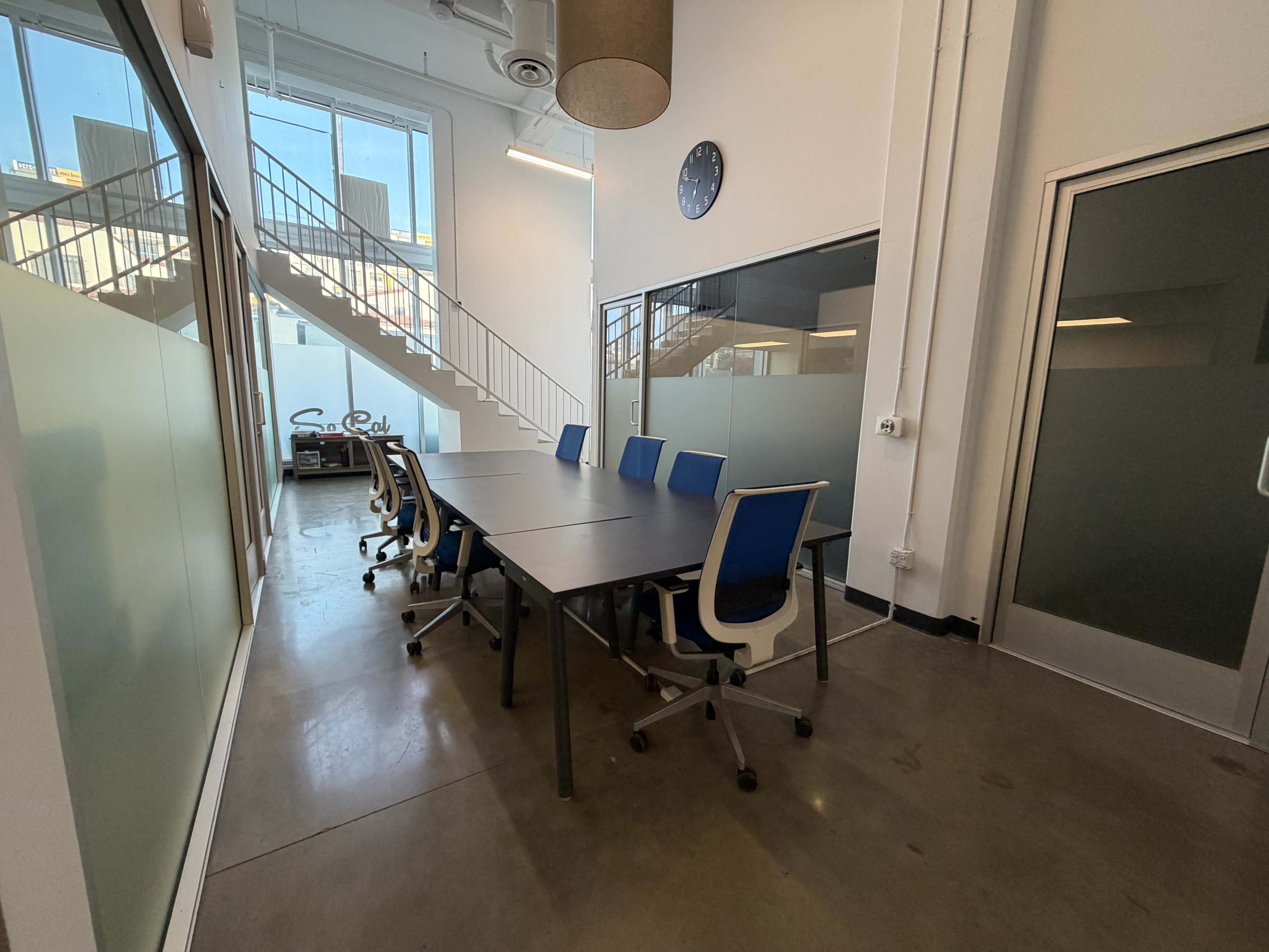 The image shows a modern conference room with a long table, several chairs, and large windows overlooking a staircase.