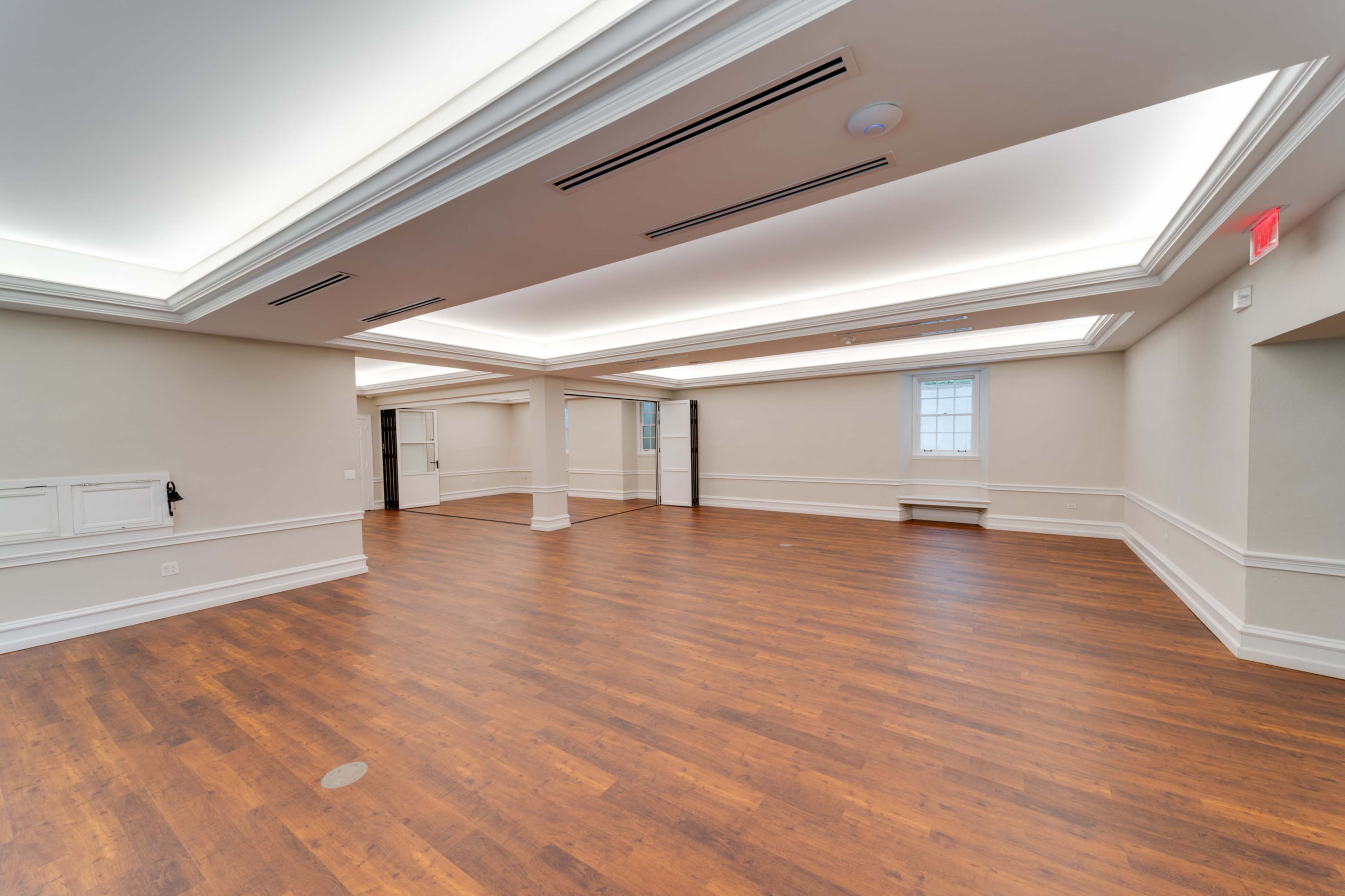 An empty room with hardwood flooring, recessed ceiling lighting, and large windows along one wall.