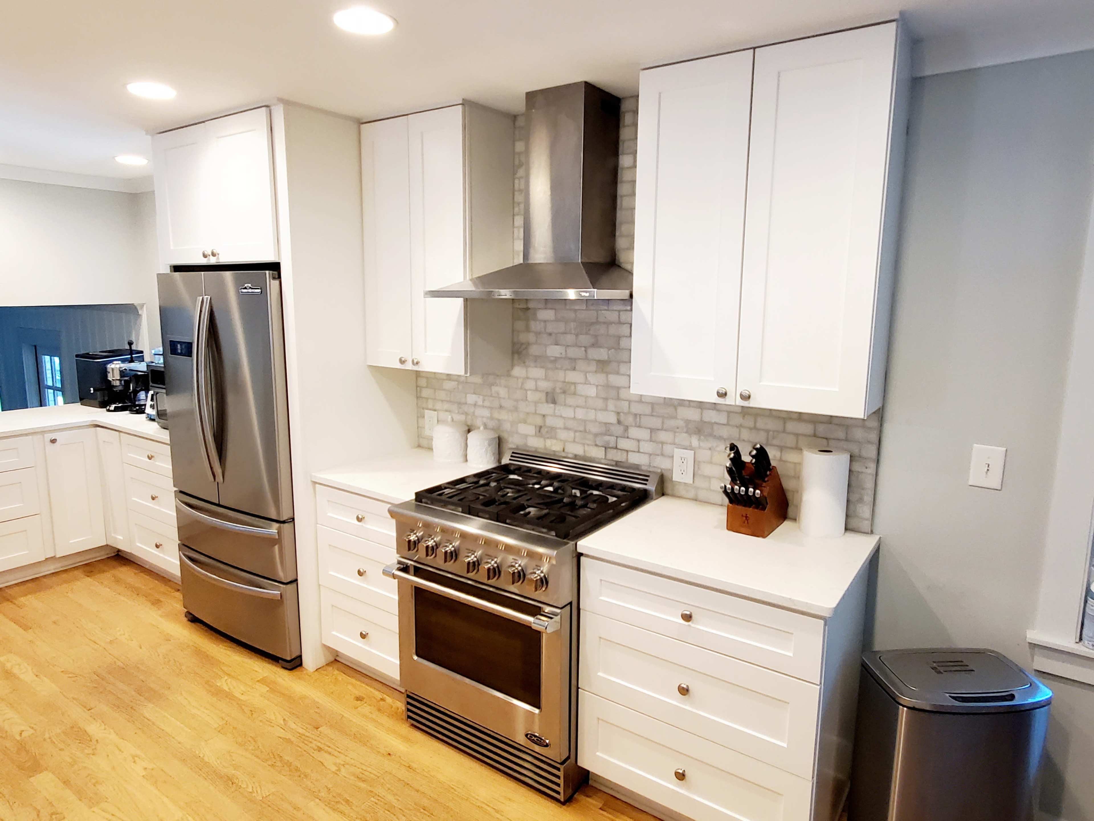 A modern kitchen features stainless steel appliances, white cabinetry, a gas range, and a backsplash of light-colored tiles.