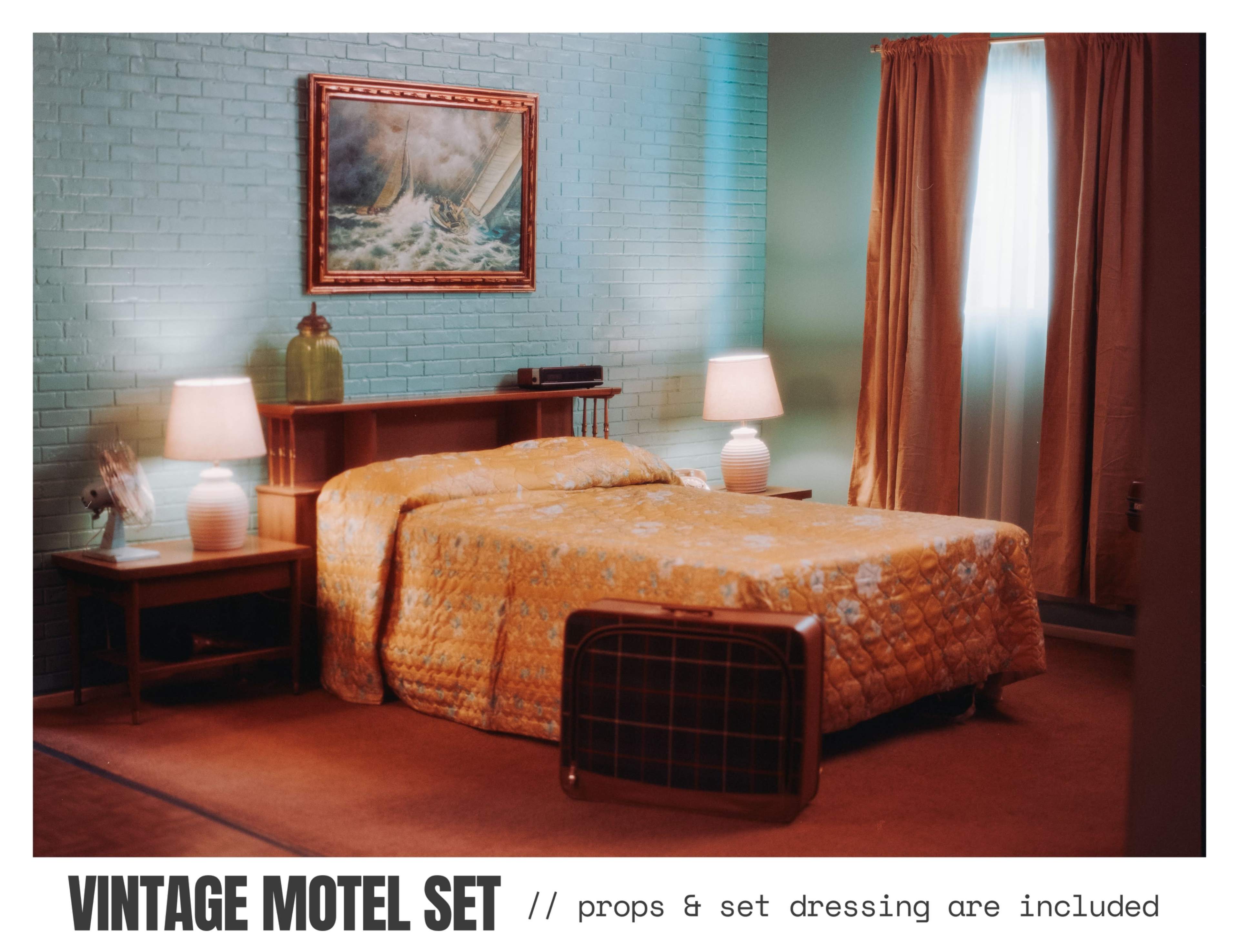 The image depicts a vintage motel room featuring a made bed with a quilt, two bedside lamps, a small table, and a framed painting on the wall.