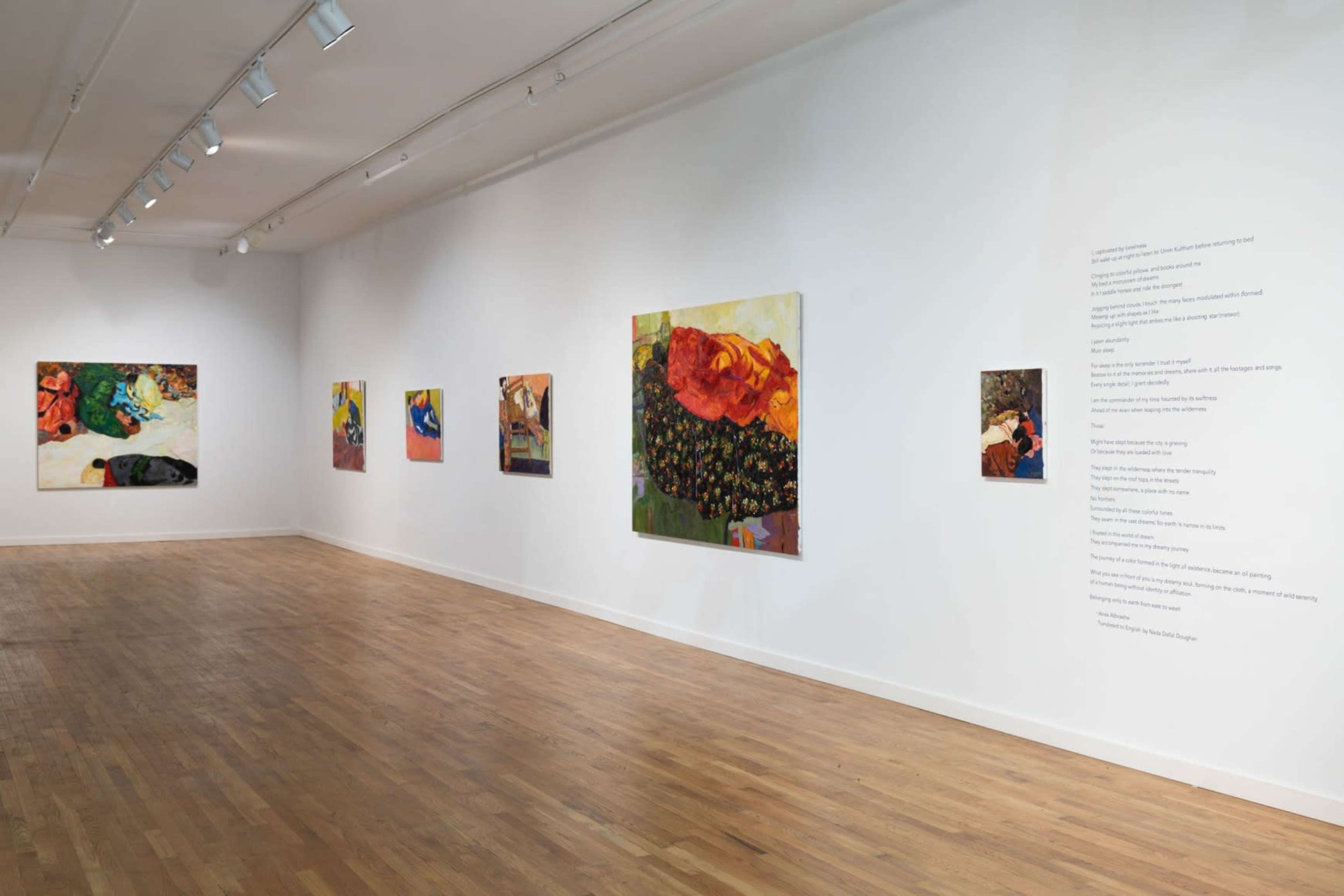 An art gallery with a wooden floor, featuring several colorful paintings displayed on the white walls.