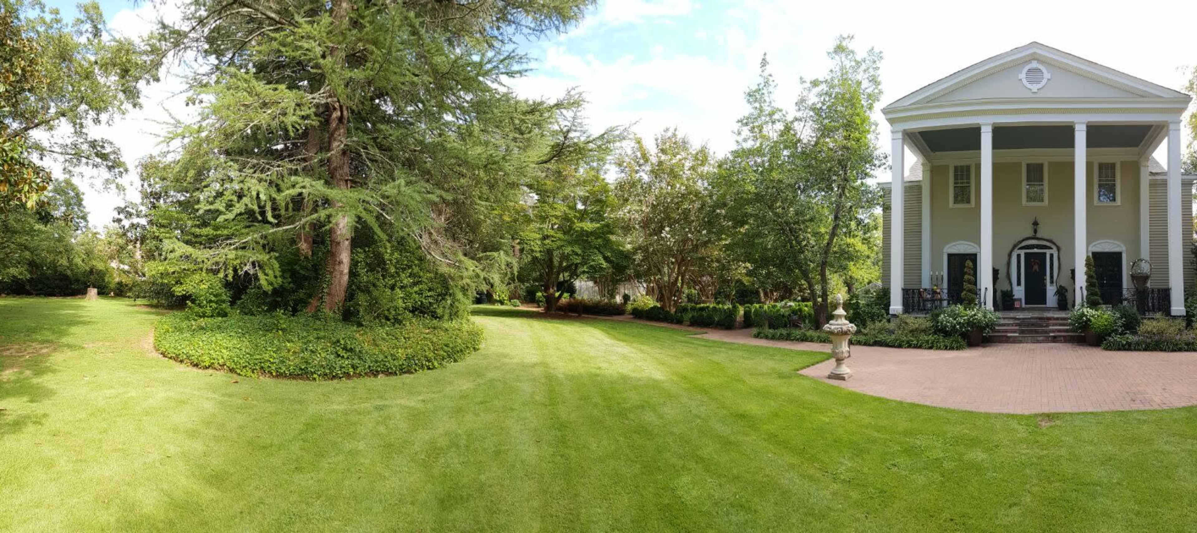 A well-maintained garden area next to a large, two-story house with a covered porch.