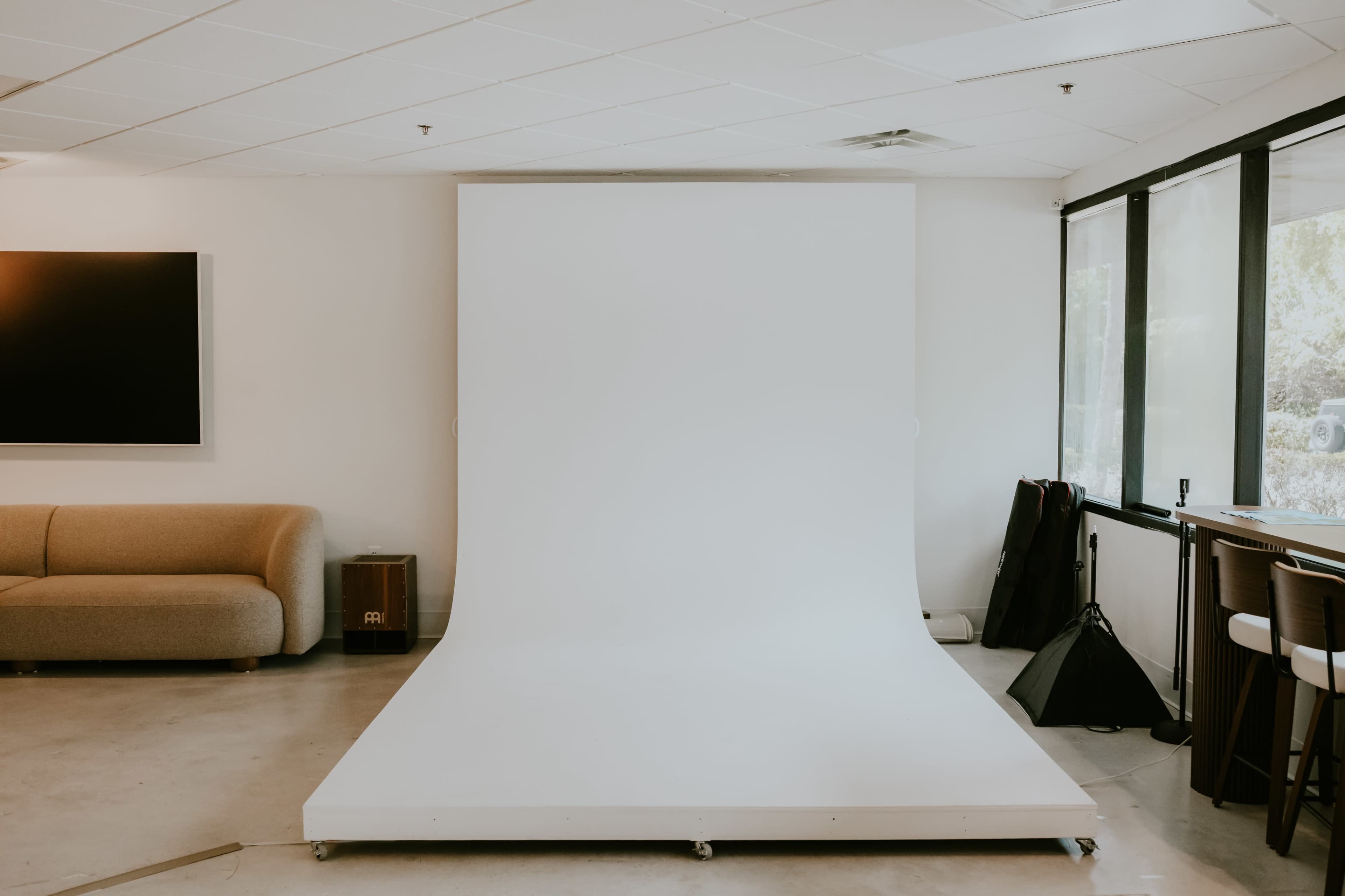The image shows a minimalistic studio setup with a large white backdrop and a sofa in a well-lit room.