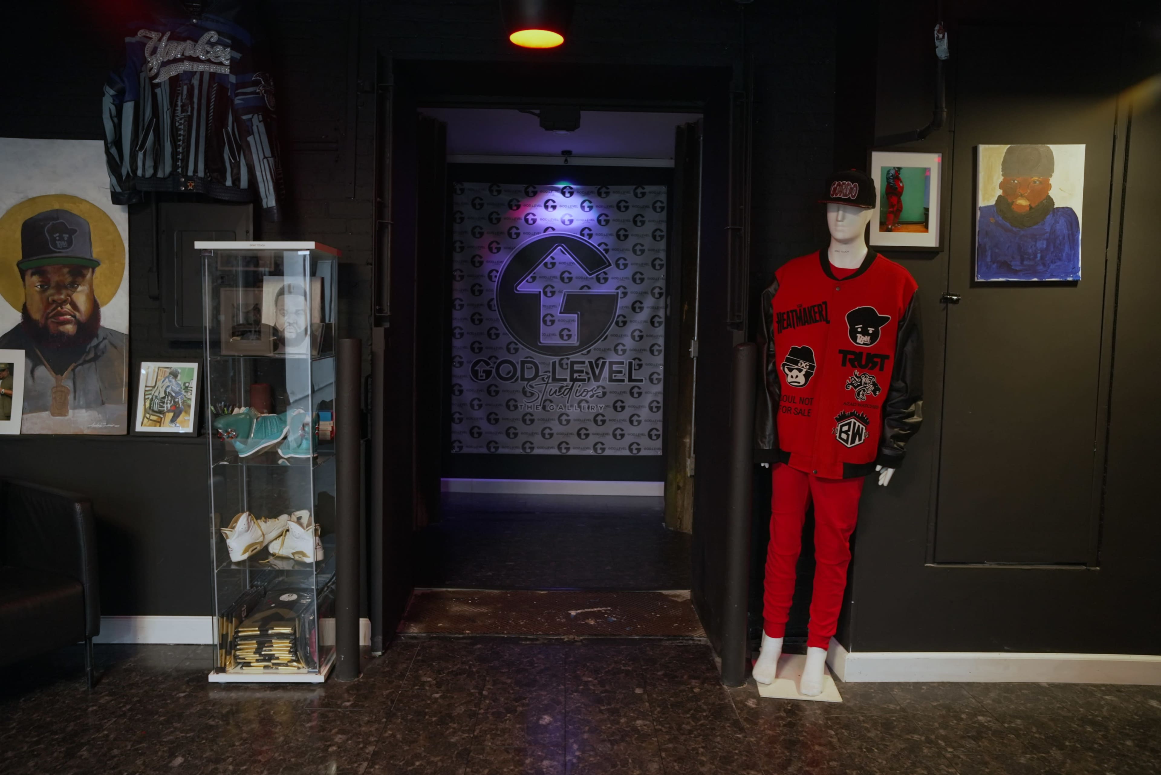 An entrance to a clothing store featuring a mannequin dressed in red and black apparel, along with artwork and a display case of items on the side.