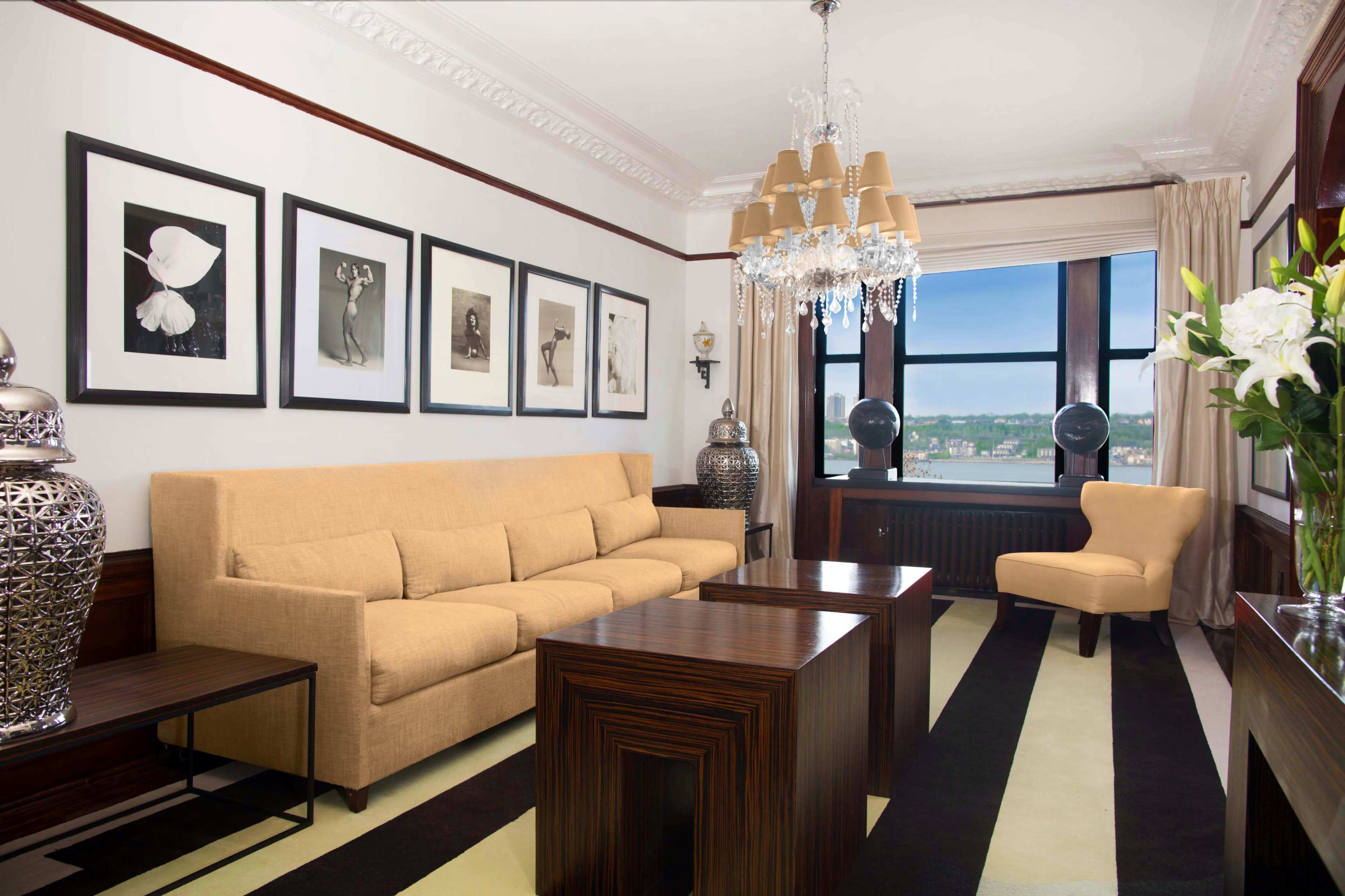 A modern living room featuring a beige sofa, wooden coffee tables, framed artwork on the walls, and large windows with a view.