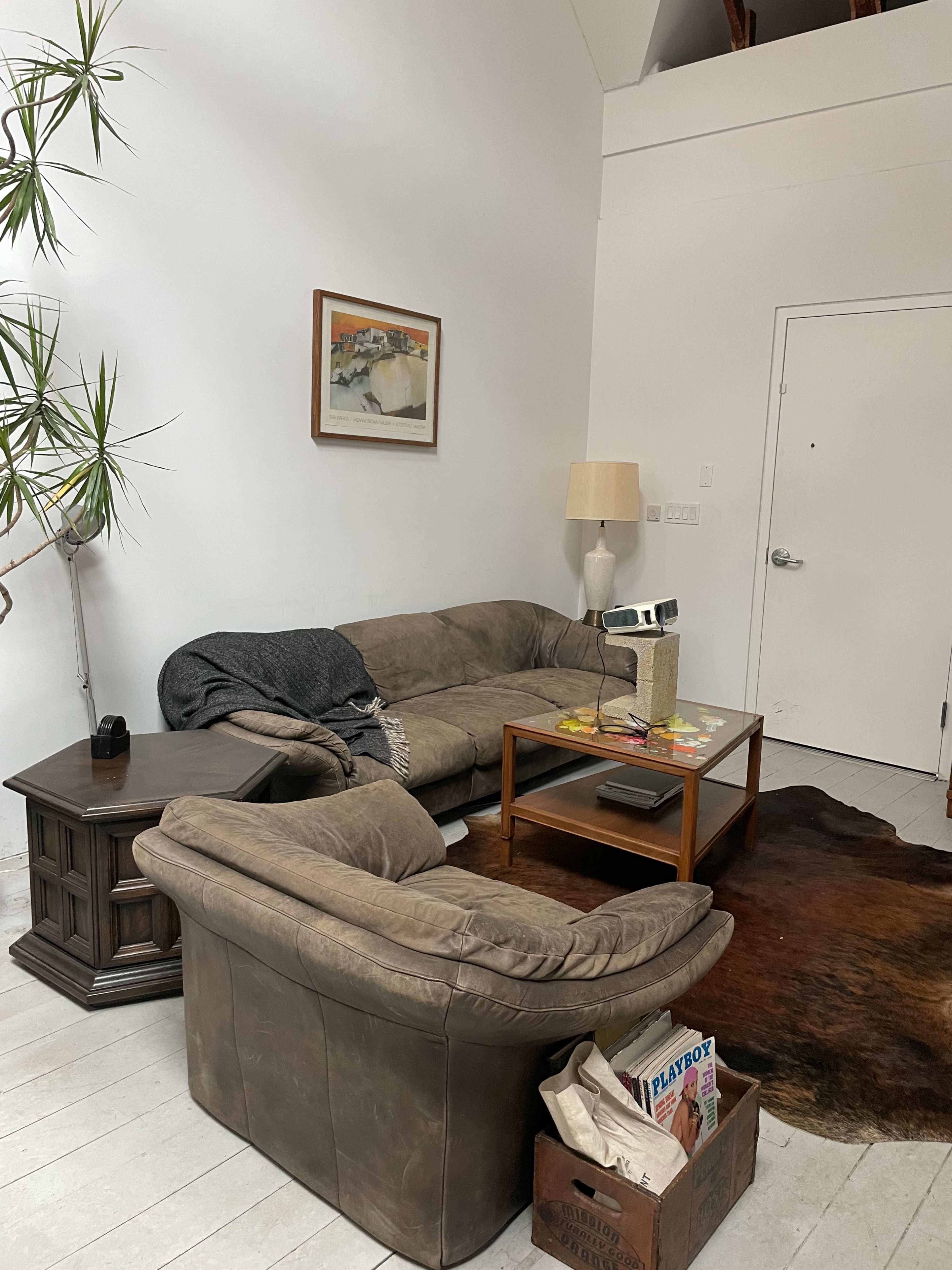 The image shows a living room with a couch, an armchair, a glass coffee table, a lamp, and a plant, all arranged around a wooden floor.
