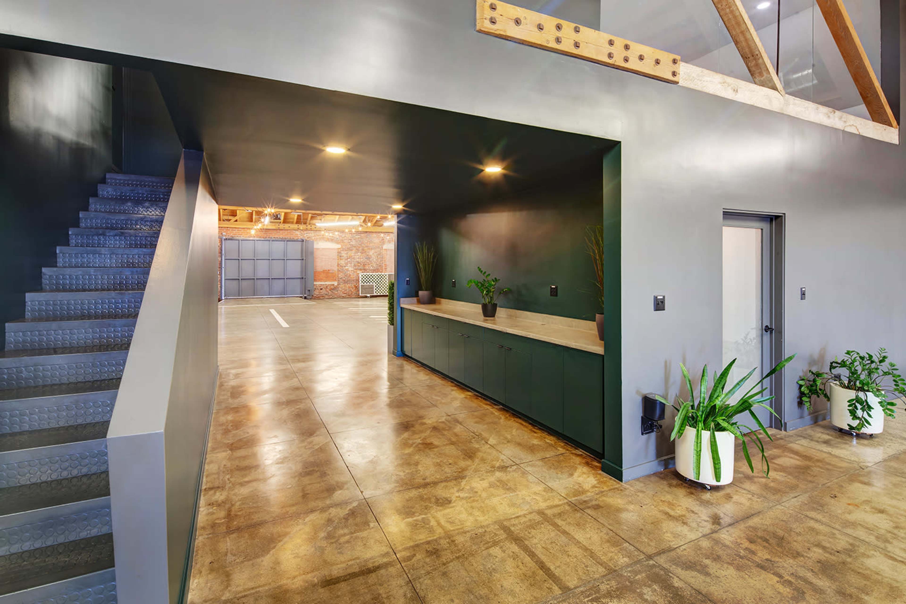 The image shows a modern interior space with a staircase leading to an upper level, a green accent wall, and potted plants along a countertop.