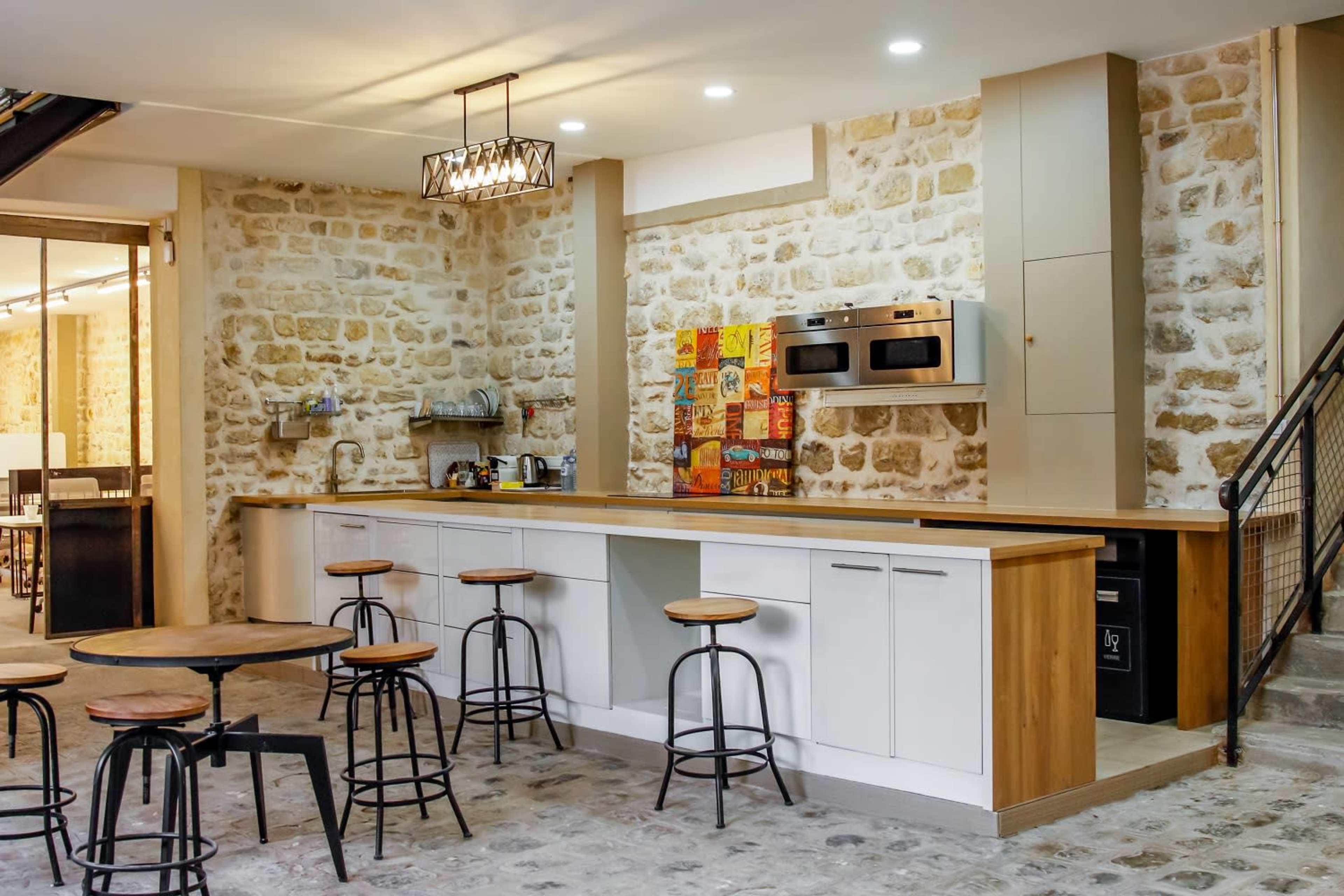 A modern kitchen with stone walls, a wooden countertop, and several stools arranged around it.