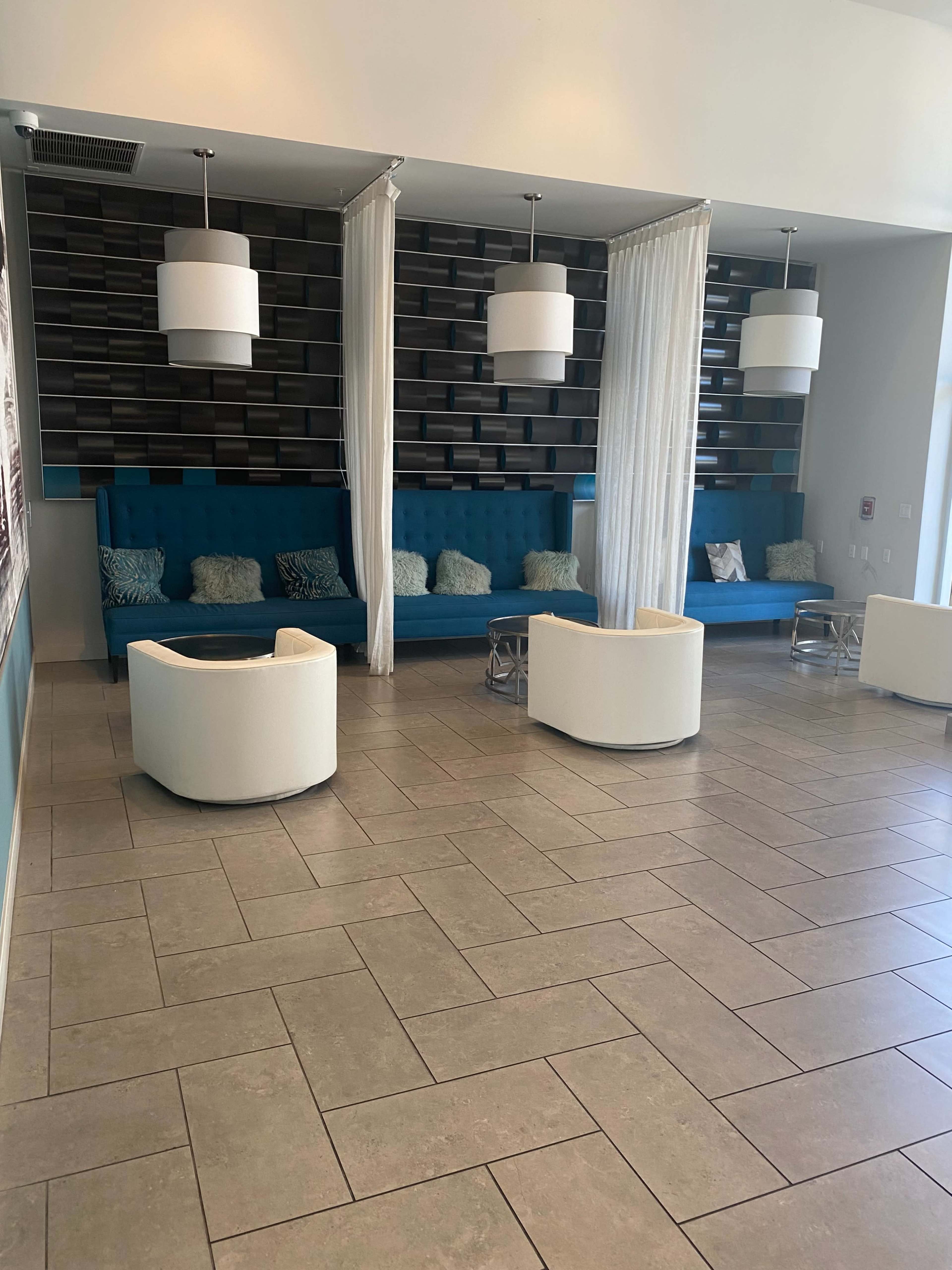 A modern lobby area with teal seating, white accent chairs, and hanging light fixtures, divided by sheer curtains.