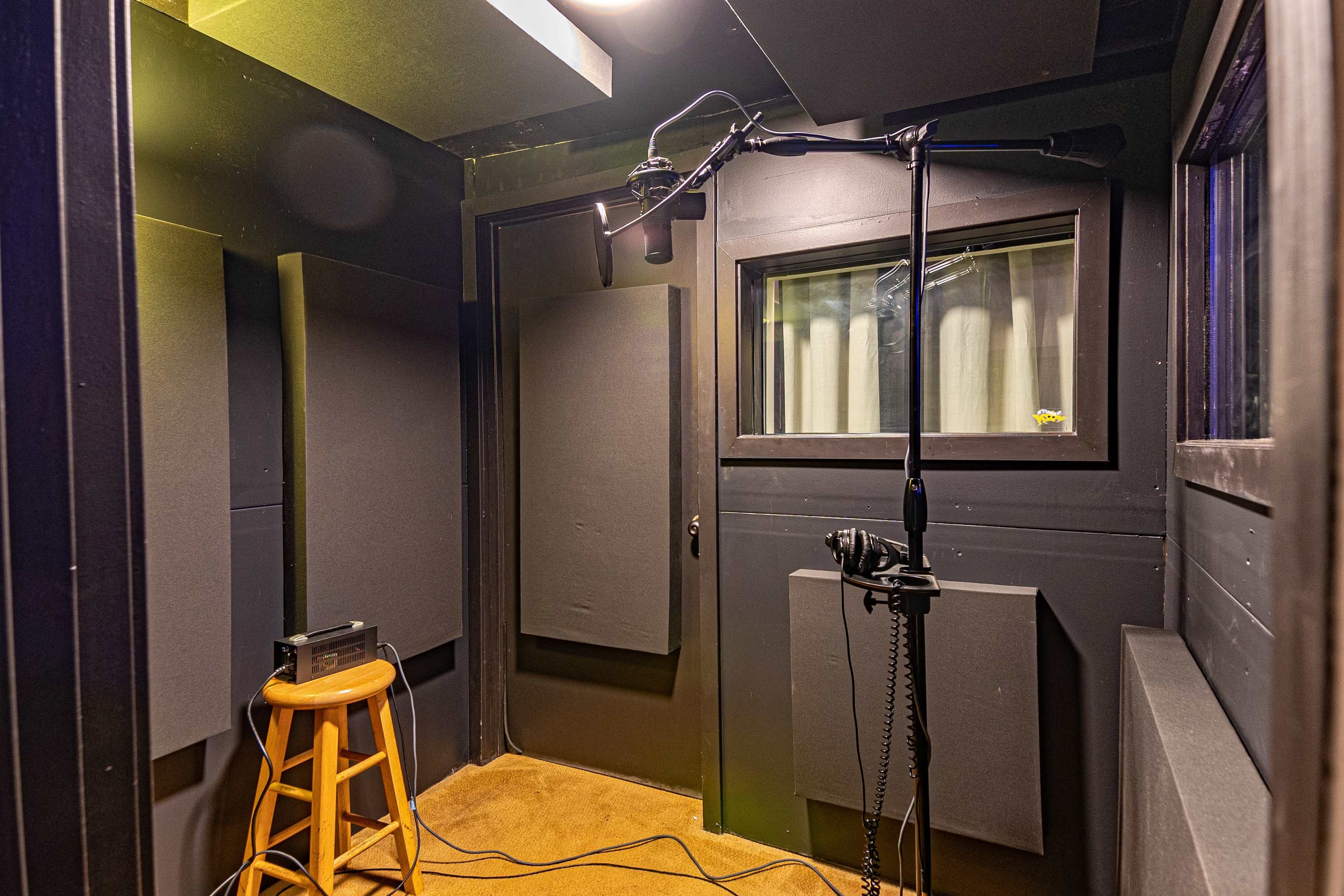A soundproof recording studio with a microphone on a stand, a stool, and padded walls.