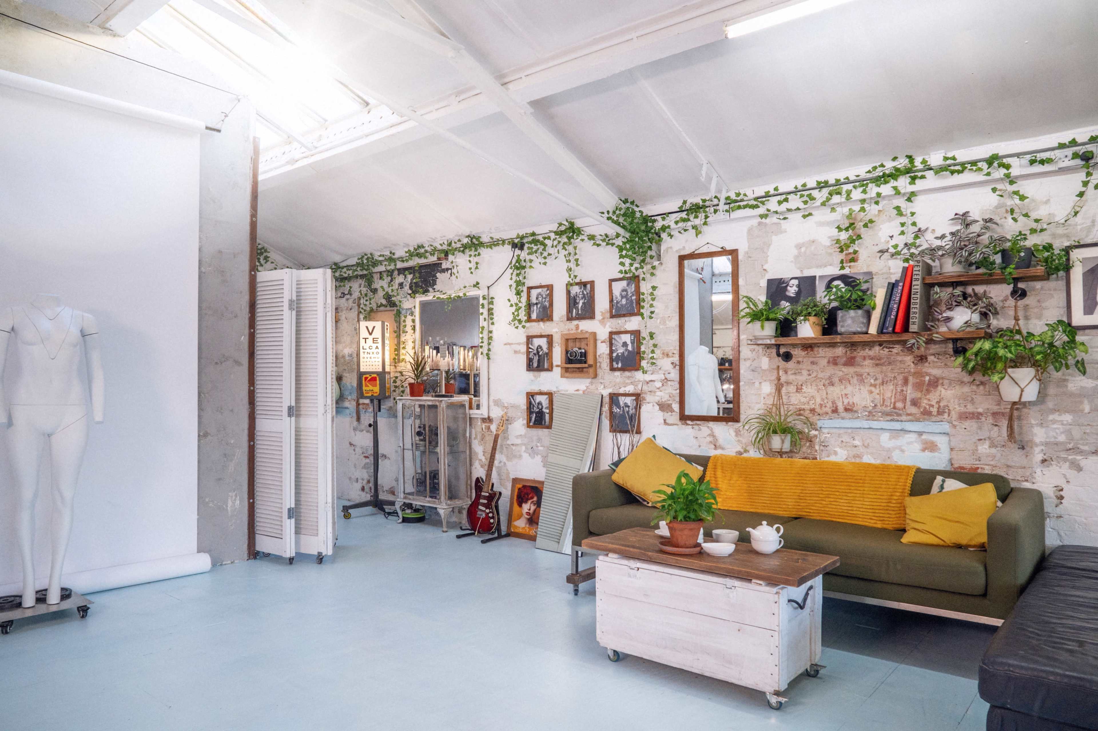 A bright and airy studio space with a green sofa, plants, framed photos on the walls, and a vintage coffee table.