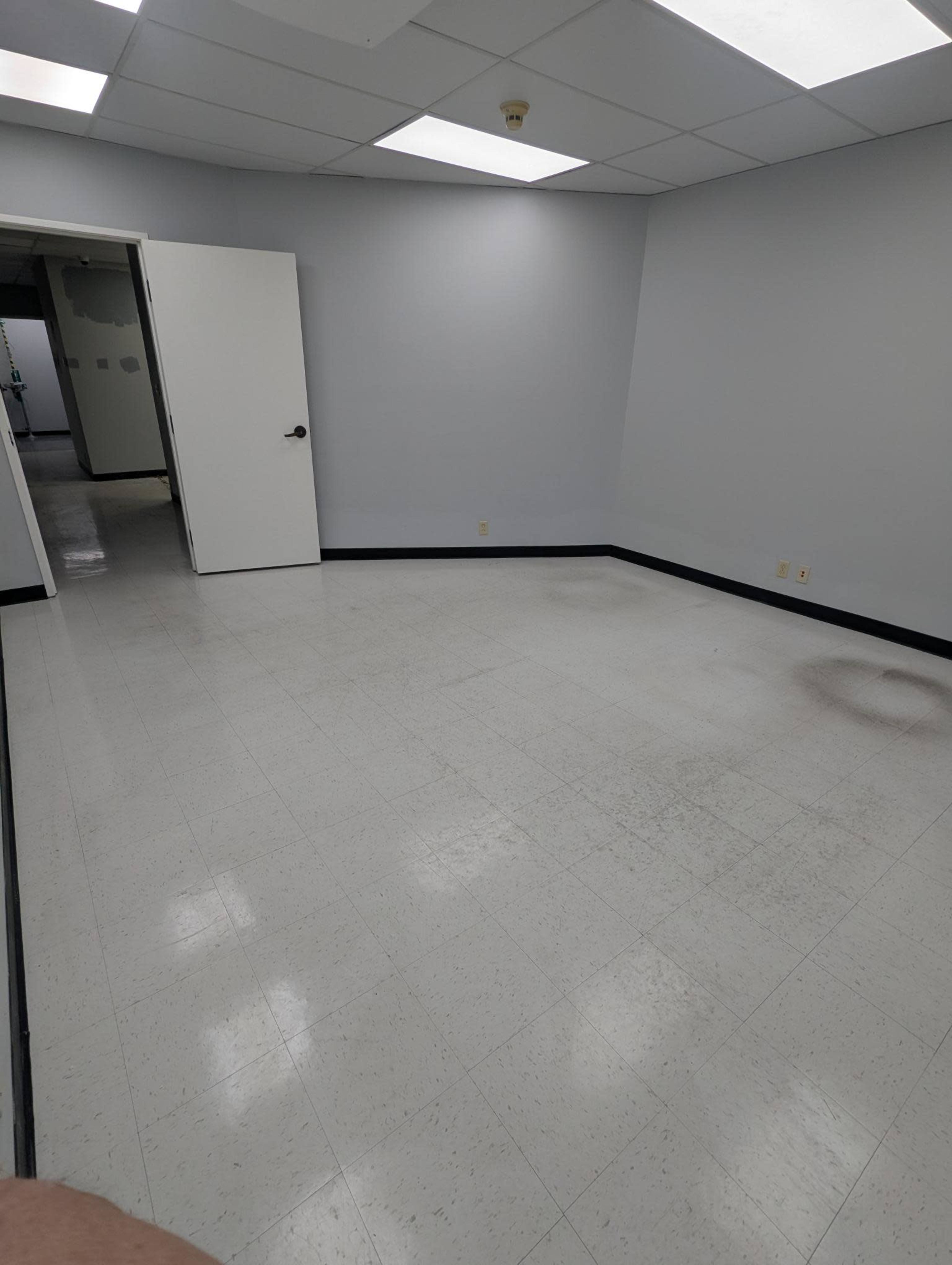 The image shows a vacant, empty room with gray walls and a white tiled floor, featuring a door that leads to another space.