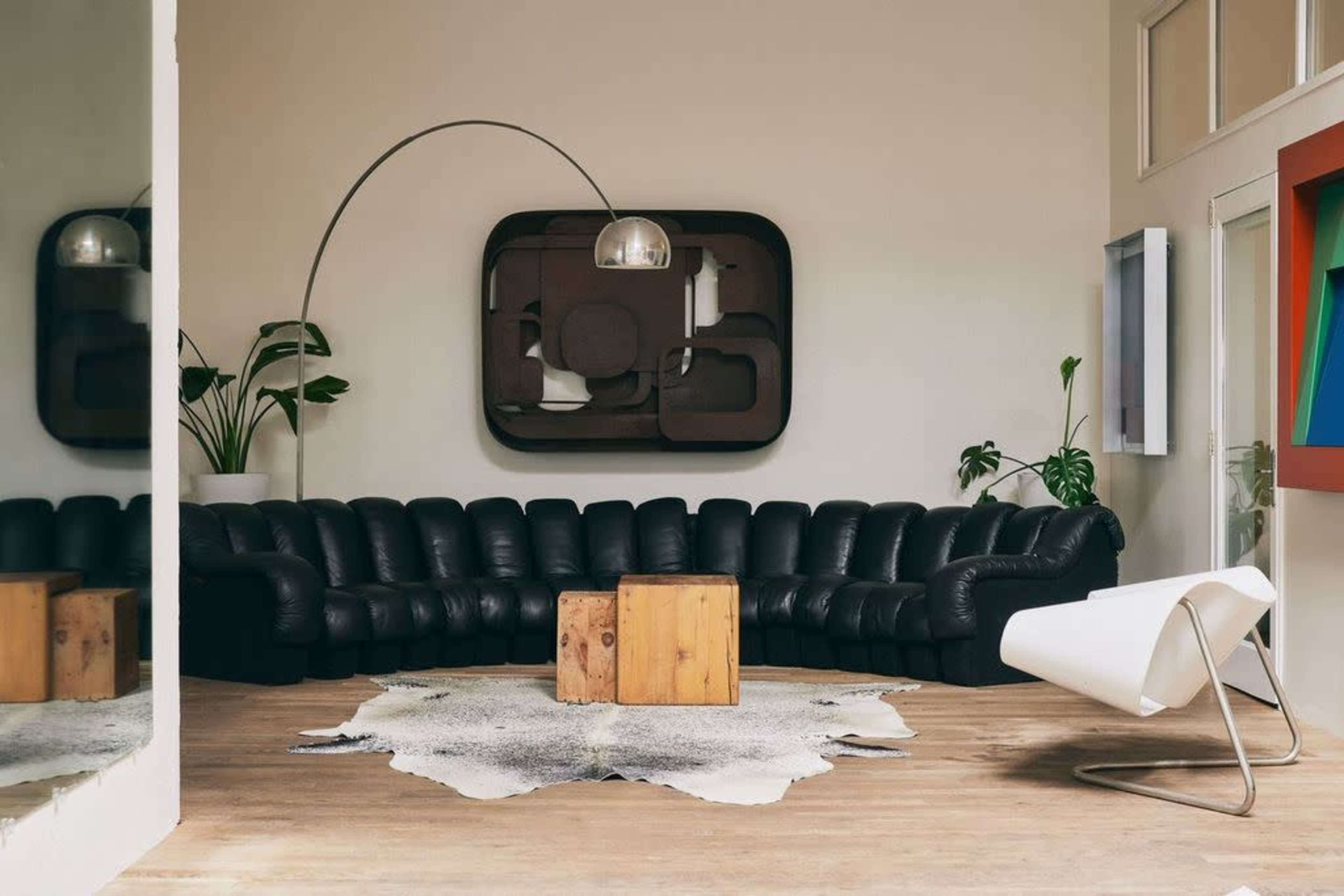 The image features a modern living room with a black curved sofa, a wooden coffee table, a large wall artwork, and indoor plants.