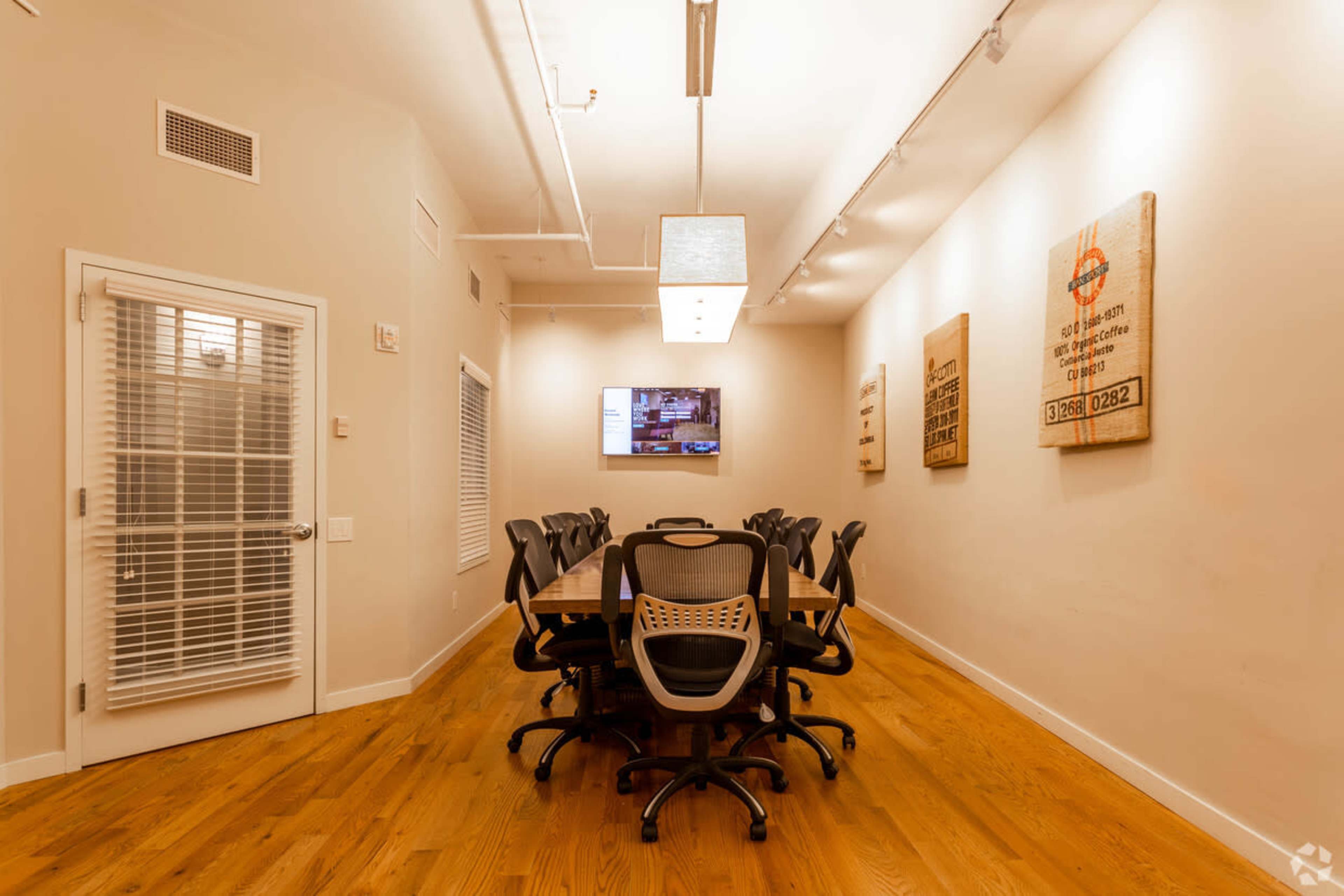 A conference room with a long wooden table, several black office chairs, a television mounted on the wall, and decorative wall art.