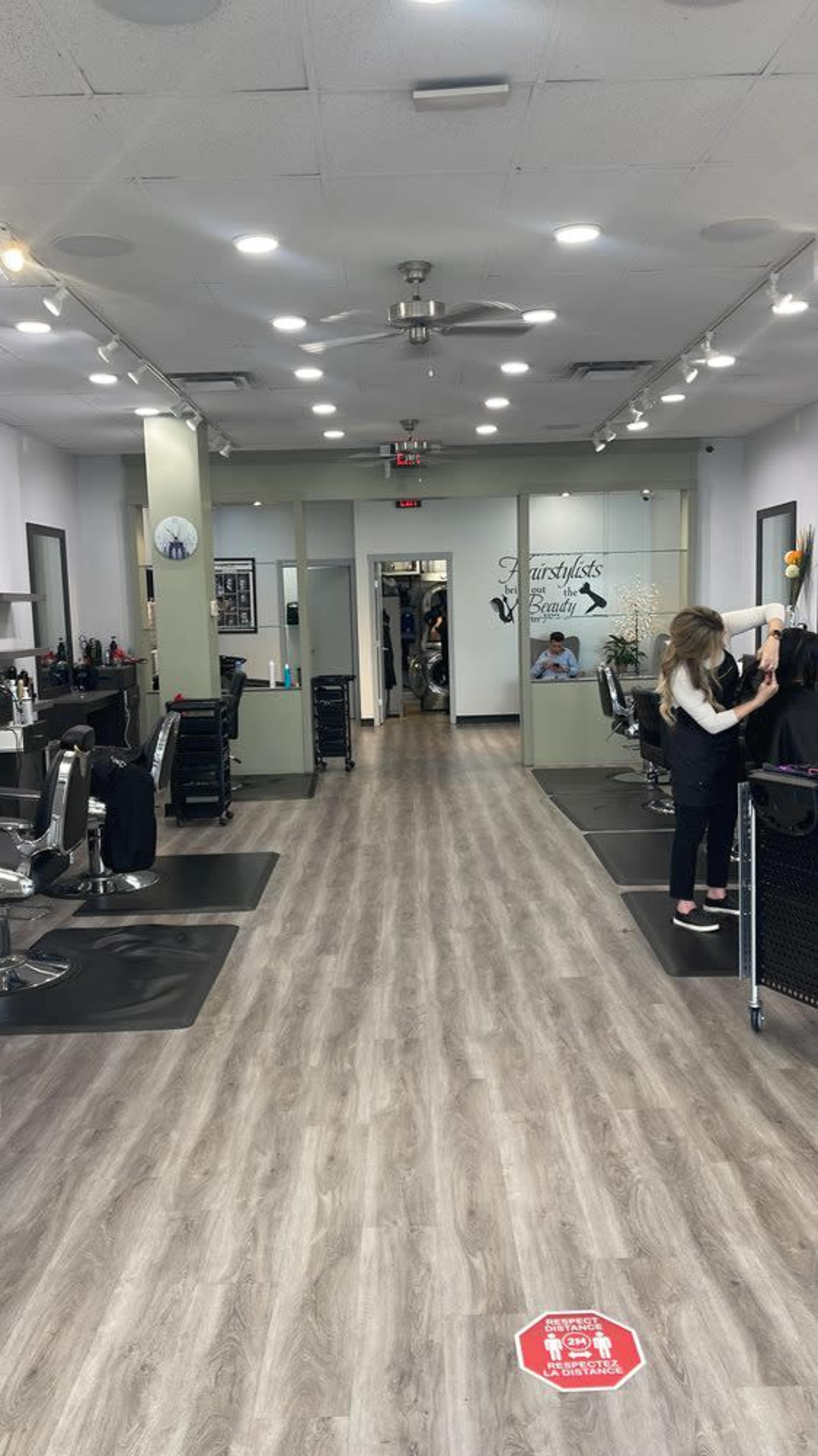 The image shows the interior of a hair salon with styling stations on either side and a reception area at the far end.