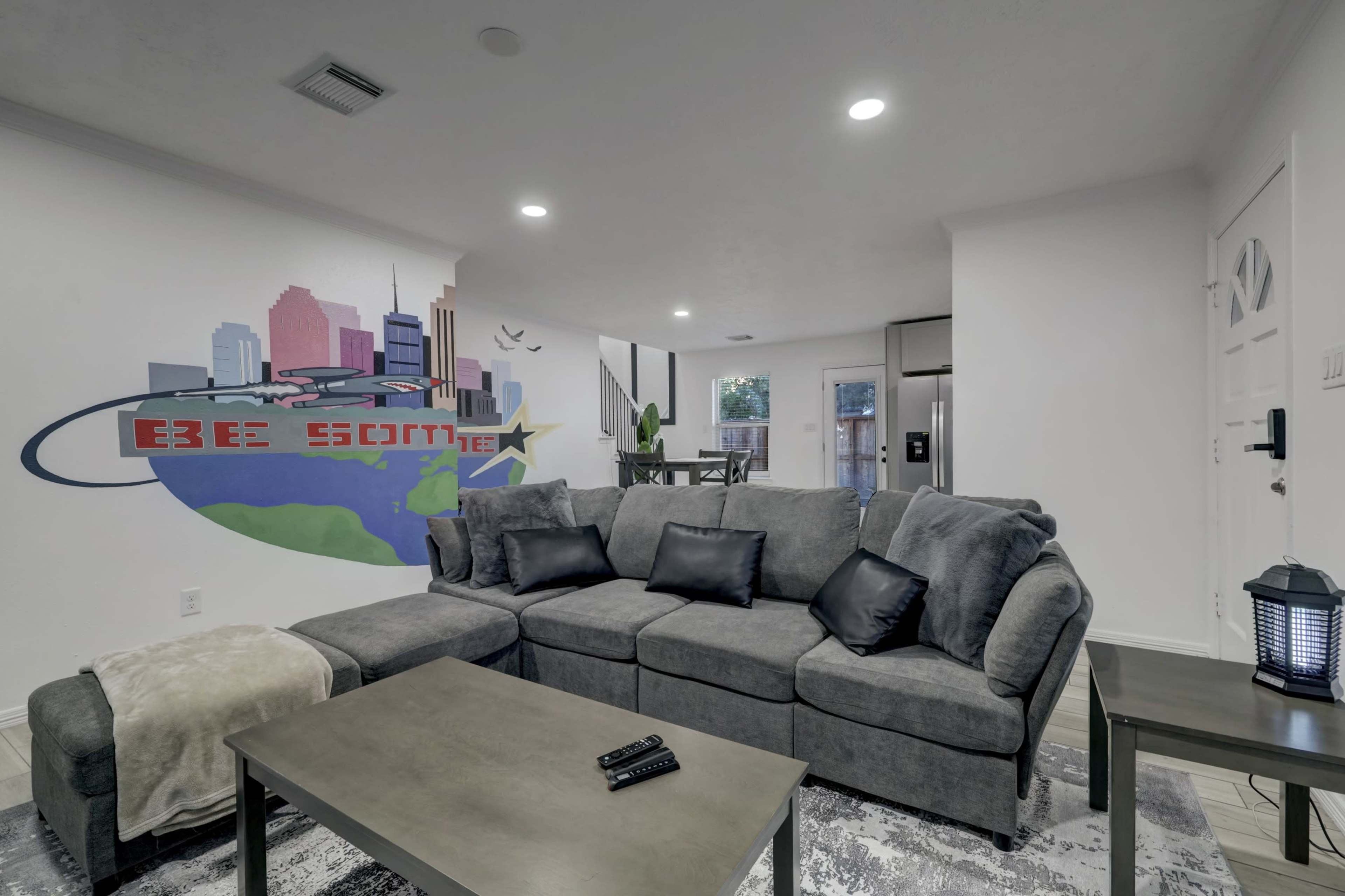 A modern living room featuring a gray sectional sofa, a coffee table, and a wall mural depicting a city skyline.