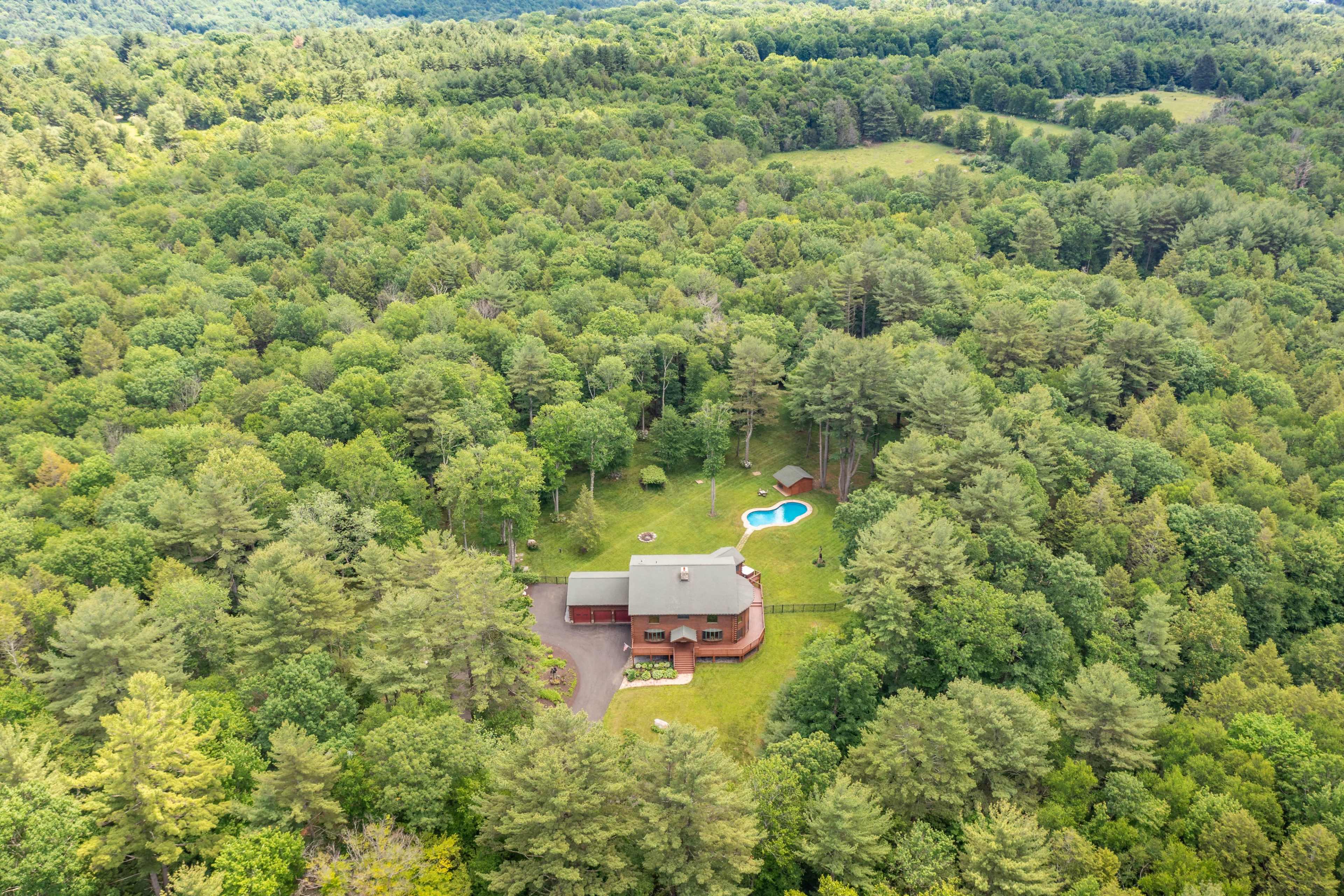 A large house with a pool is situated in the middle of a dense forested area.
