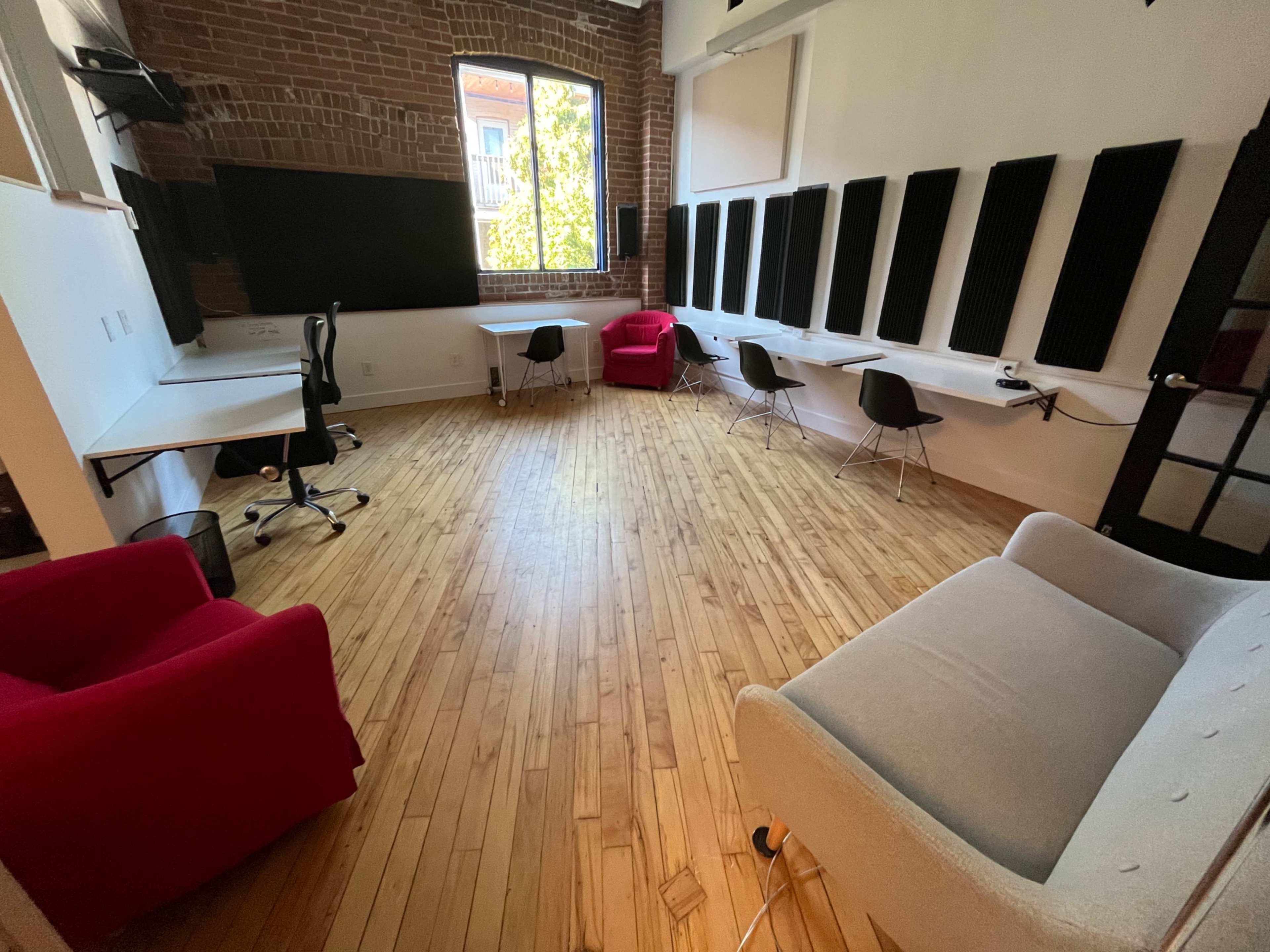 The room features hardwood flooring, a large window, and is furnished with several chairs and tables, alongside sound-absorbing panels on the walls.