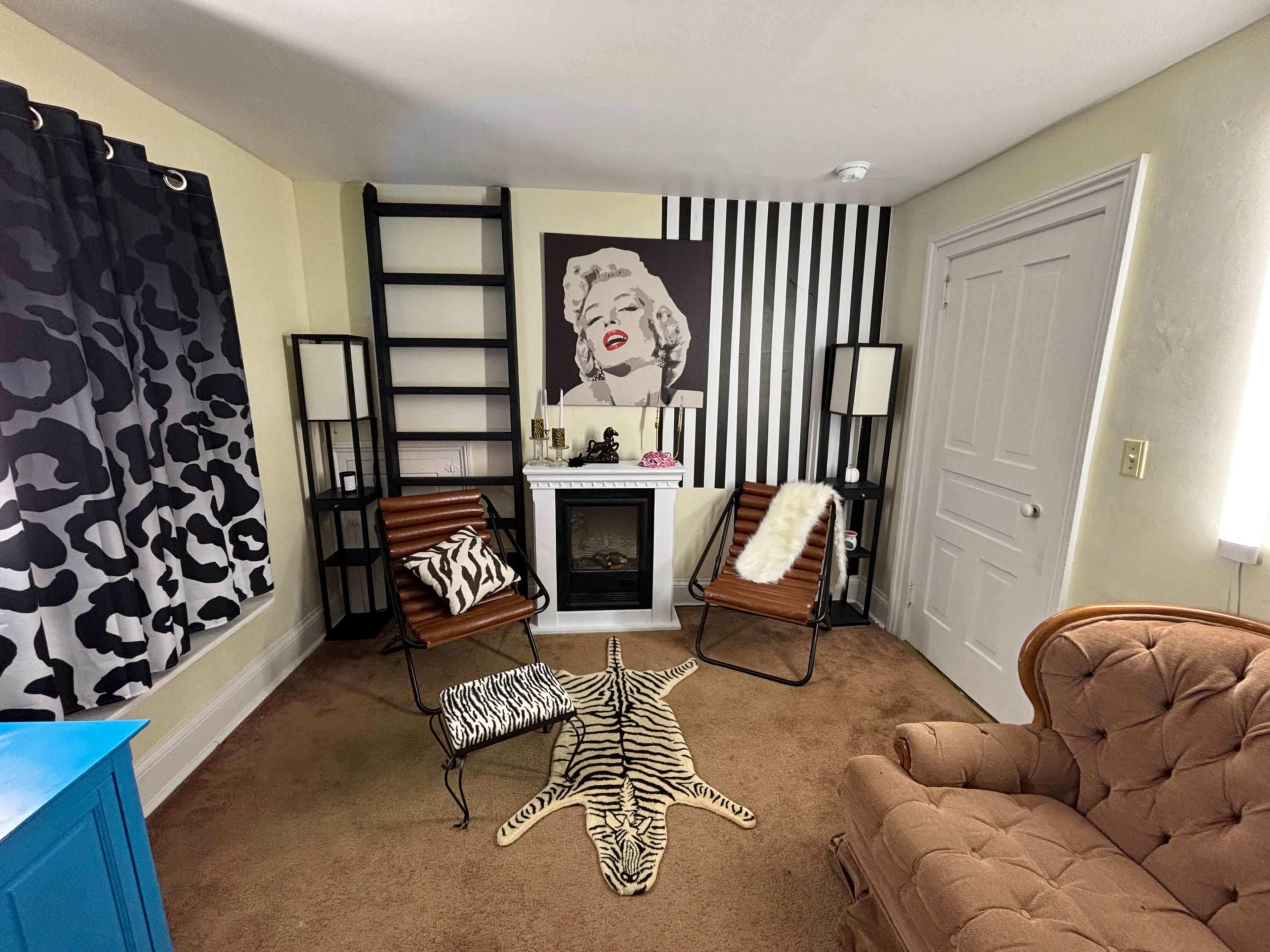 The room features a cozy seating area with a brown couch, two striped chairs, a black and white striped wall, and a decorative zebra-striped rug on the floor.