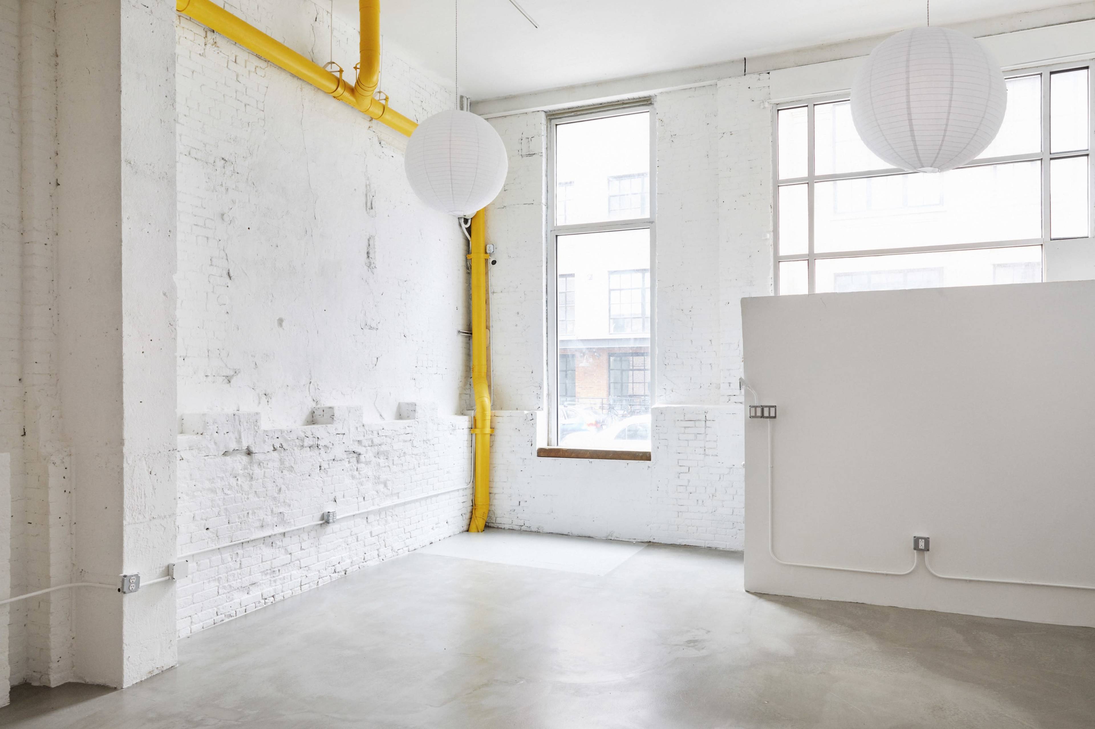 A spacious, minimalist room with white brick walls, large windows, and hanging paper lanterns.