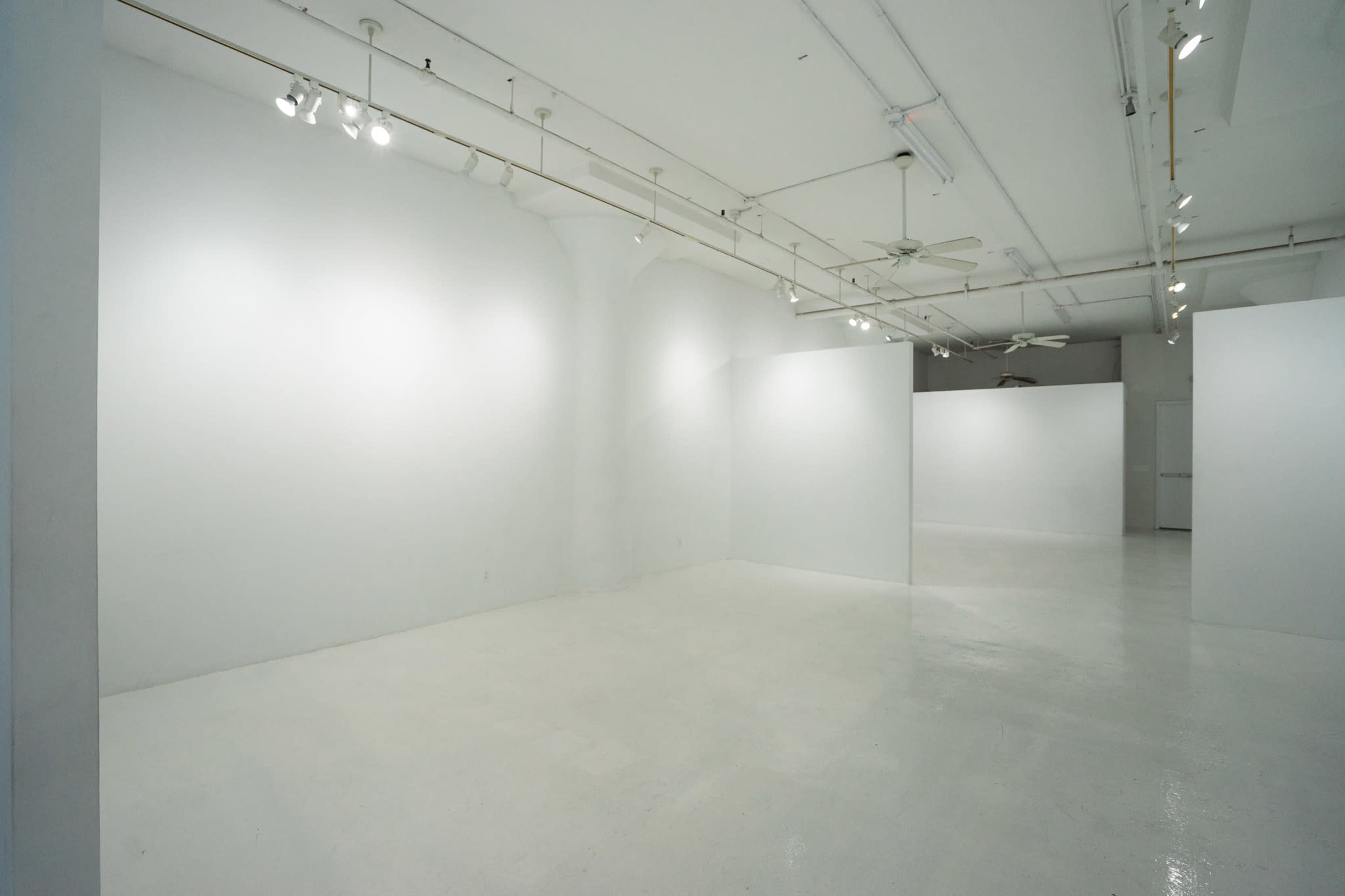 The image shows an empty, well-lit art gallery with white walls and a polished floor.
