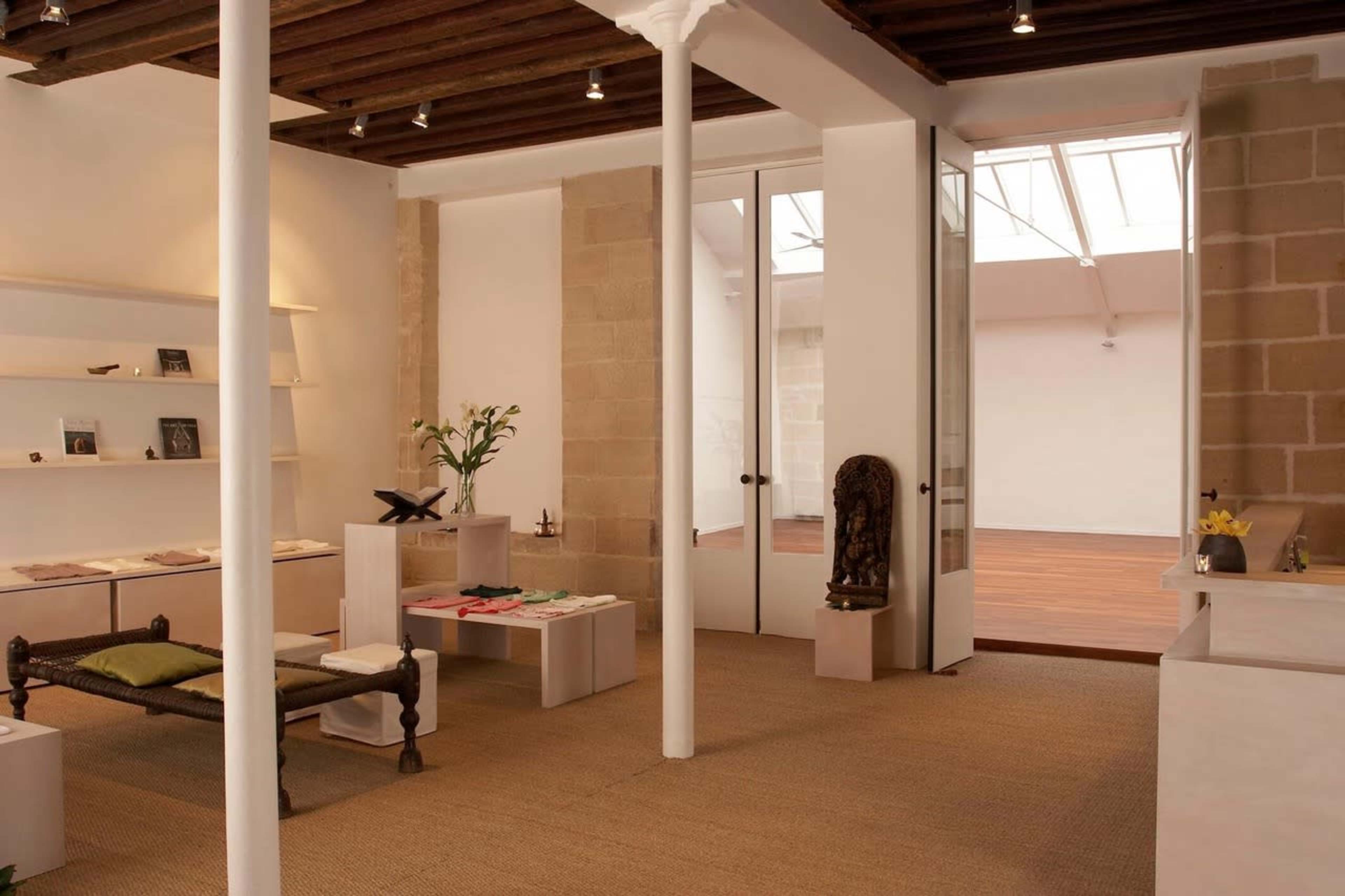 A spacious gallery-like interior with light-colored walls, wood accents, and a few minimalist display shelves and furniture pieces.