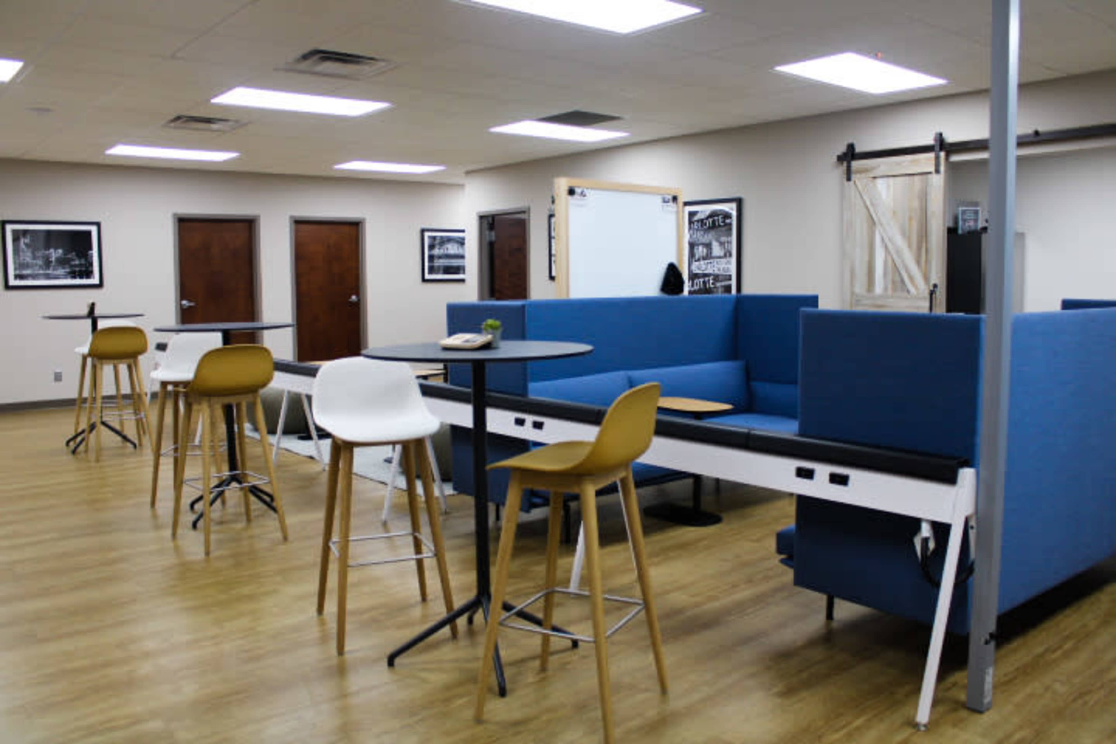 A modern lounge area with blue seating, black and wooden tables, and bright overhead lights in a spacious room.