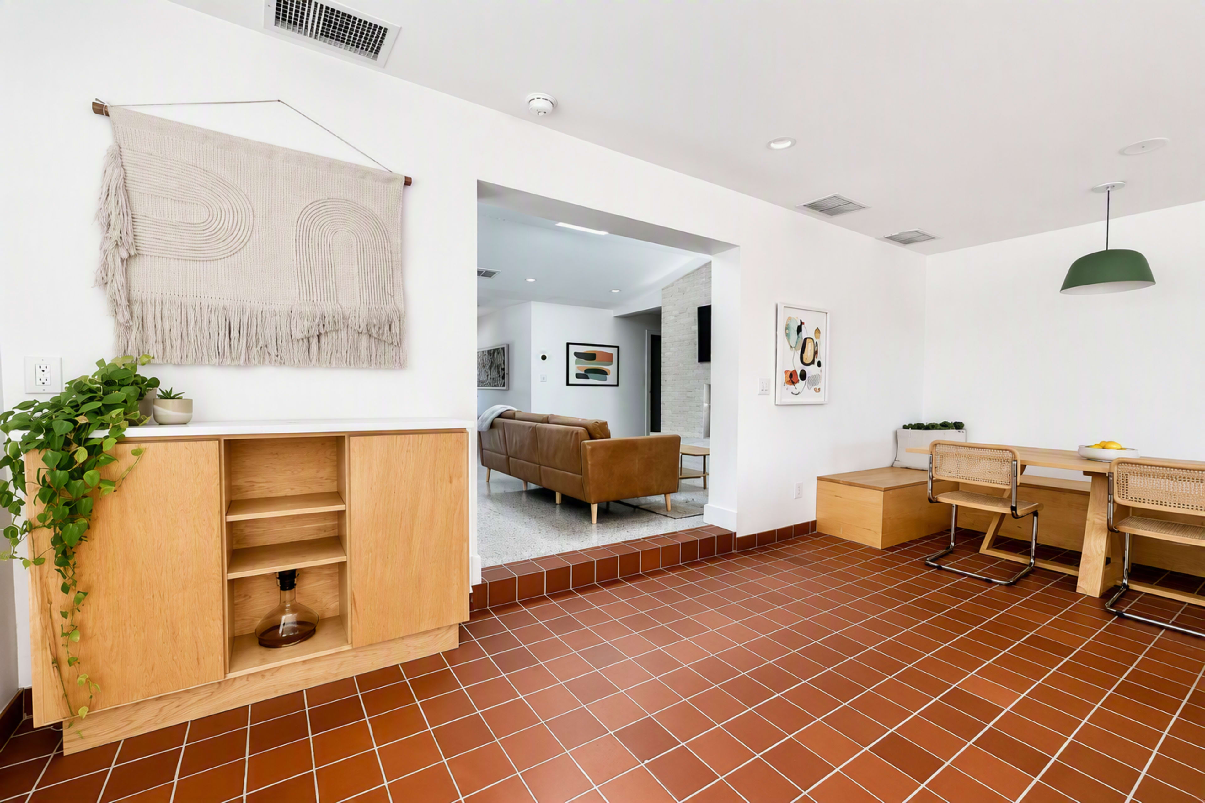 The image features a modern interior space with a tile floor, a wooden cabinet, and a dining area that includes a table and chairs, while a living area is visible in the background.