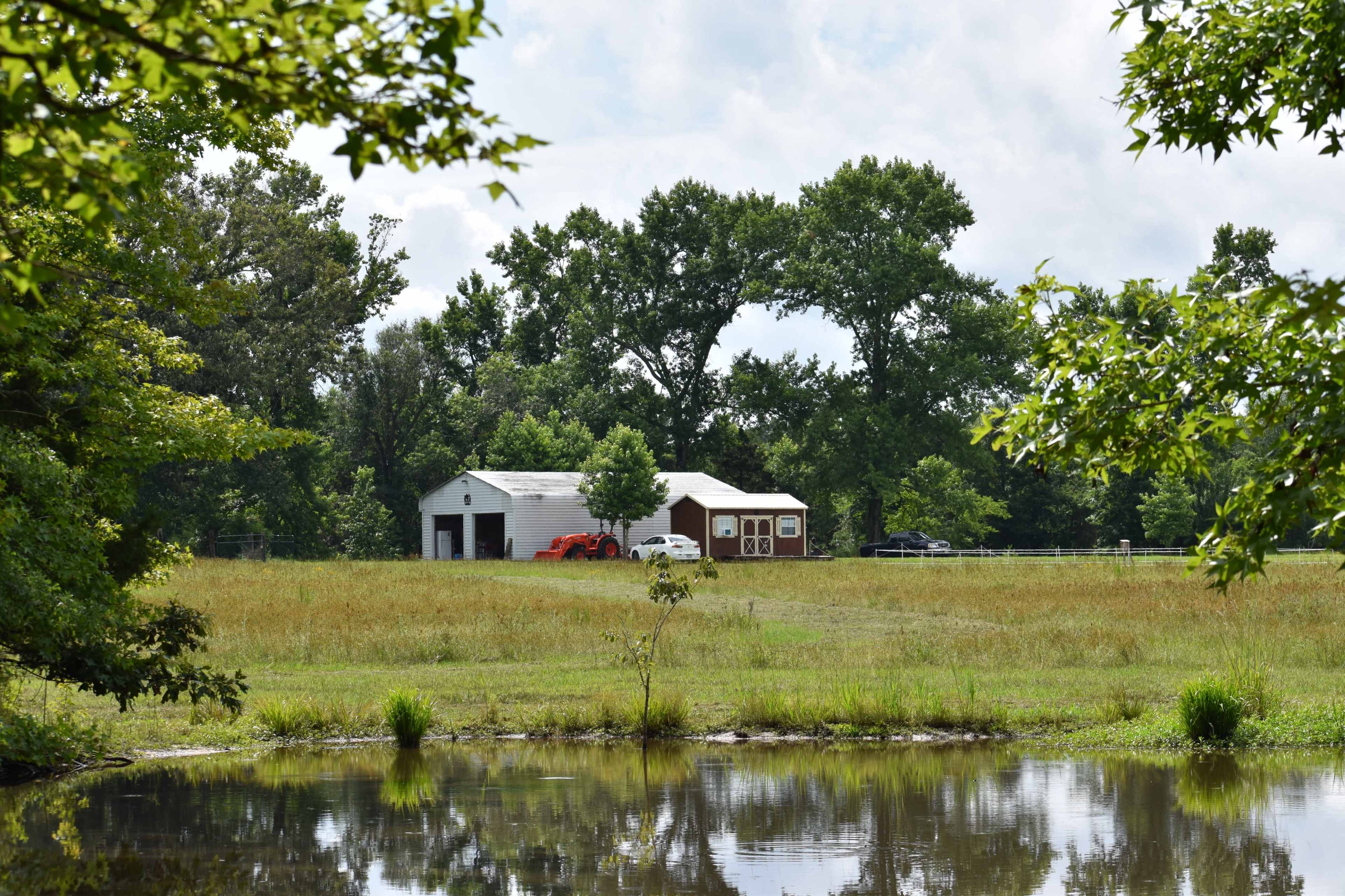 A red vehicle is parked near a barn-style building on a grassy field with a pond in the foreground.