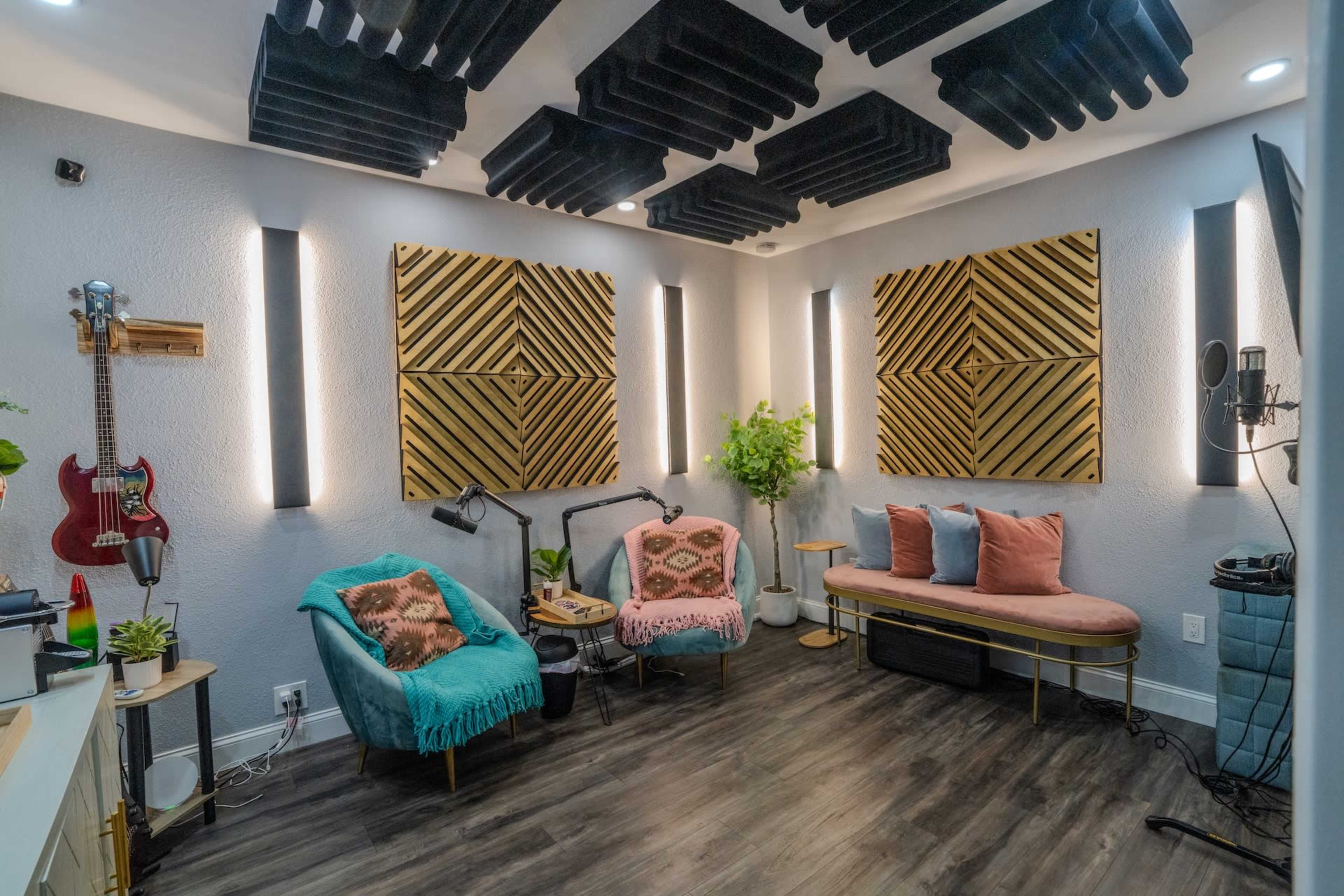 The image shows a soundproofed recording studio with acoustic panels on the walls, a microphone setup, and comfortable seating arrangements.