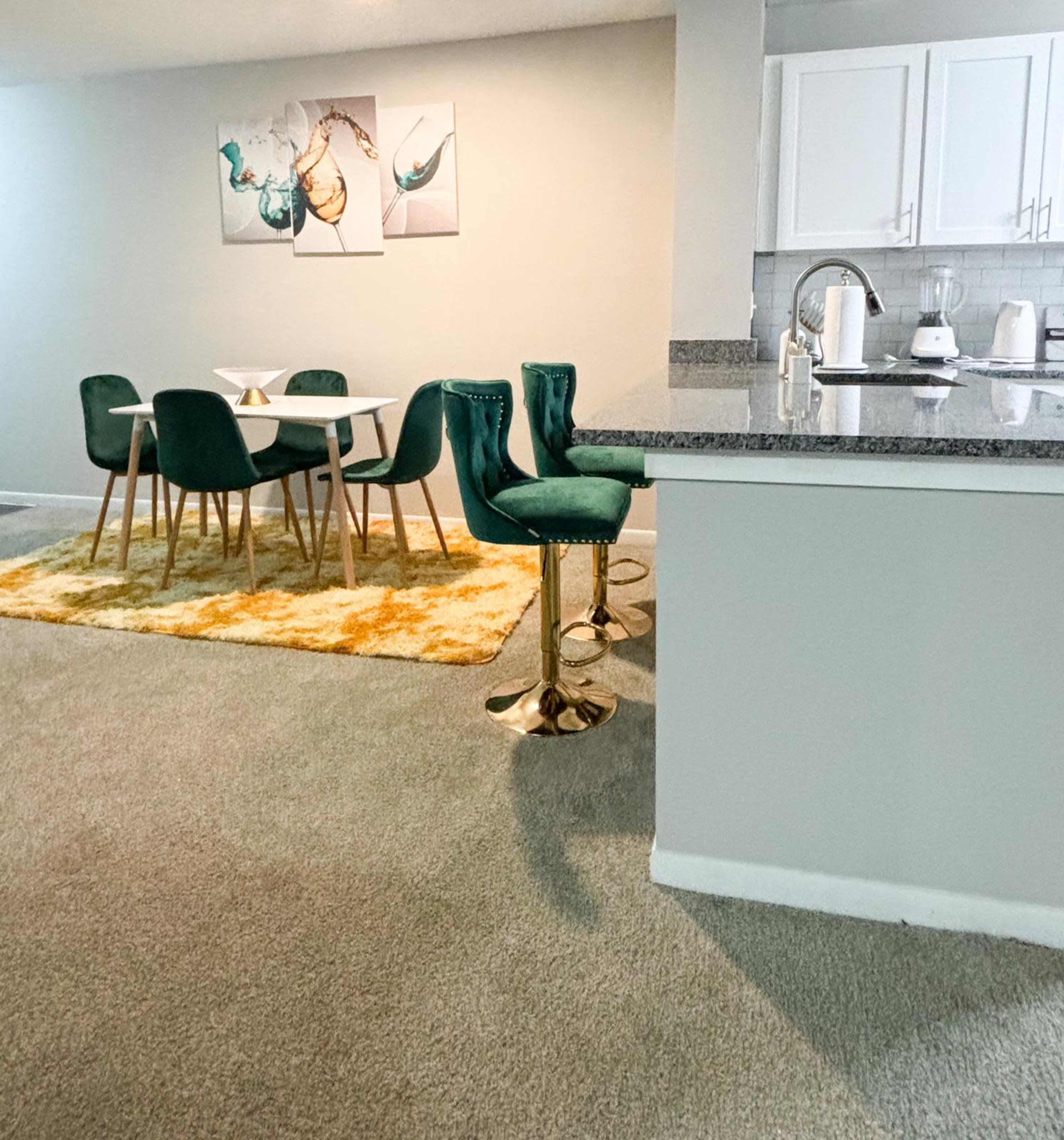 A modern dining area with a white table and green chairs, complemented by a bright yellow rug, all set against a neutral-colored wall.