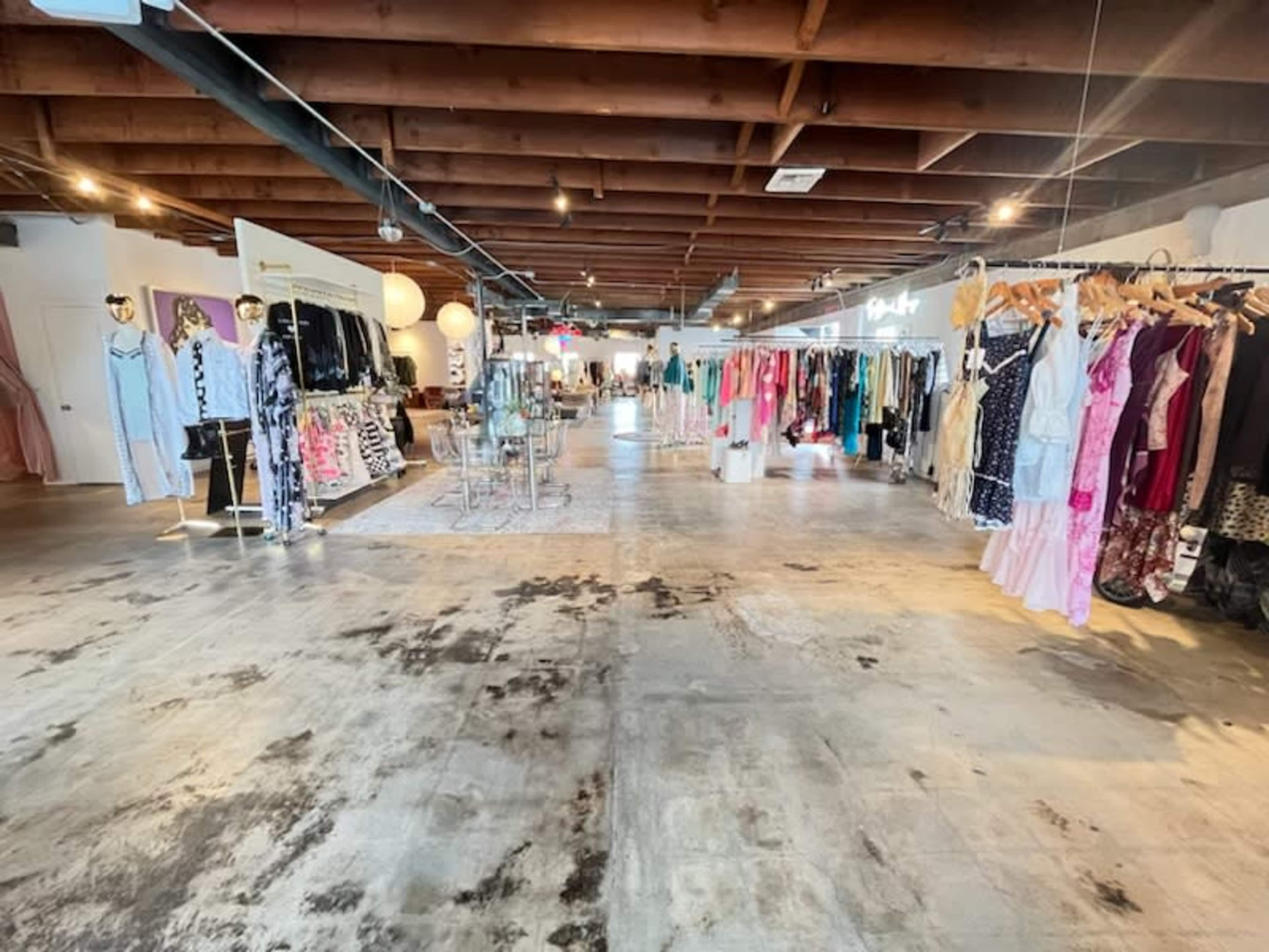 A spacious retail store with clothing racks on either side and a well-lit, polished concrete floor.