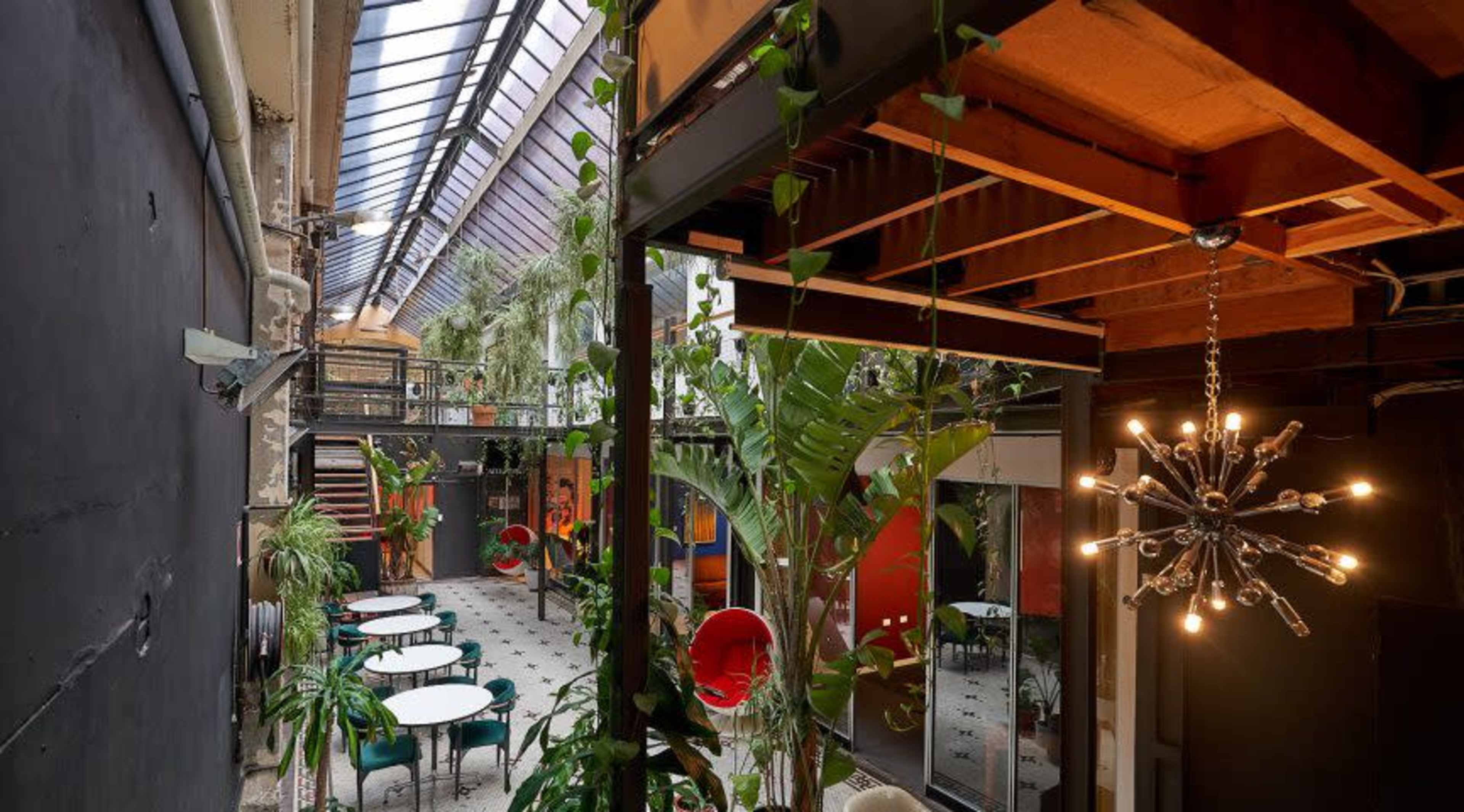 An indoor space with a high glass ceiling, featuring a mix of greenery, modern furniture, and artistic decor.