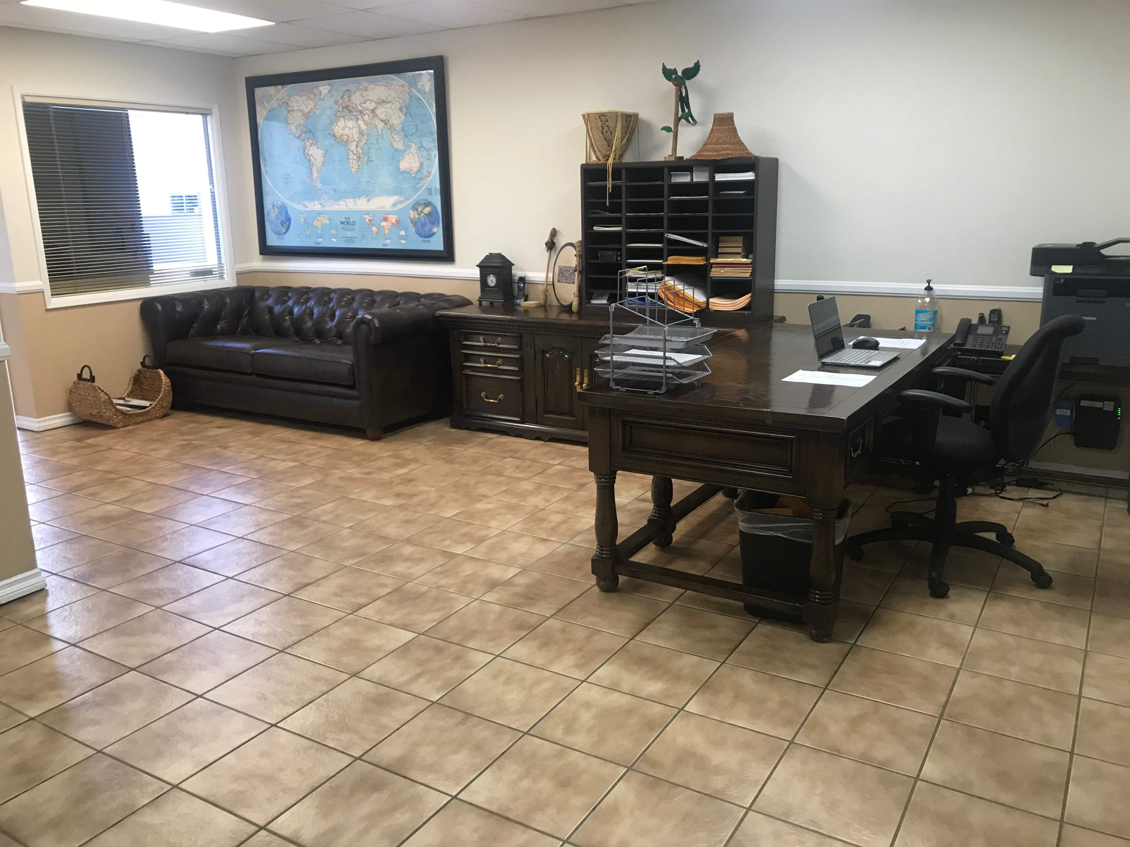 A spacious office with a leather couch, a large desk with a computer, and a world map on the wall.