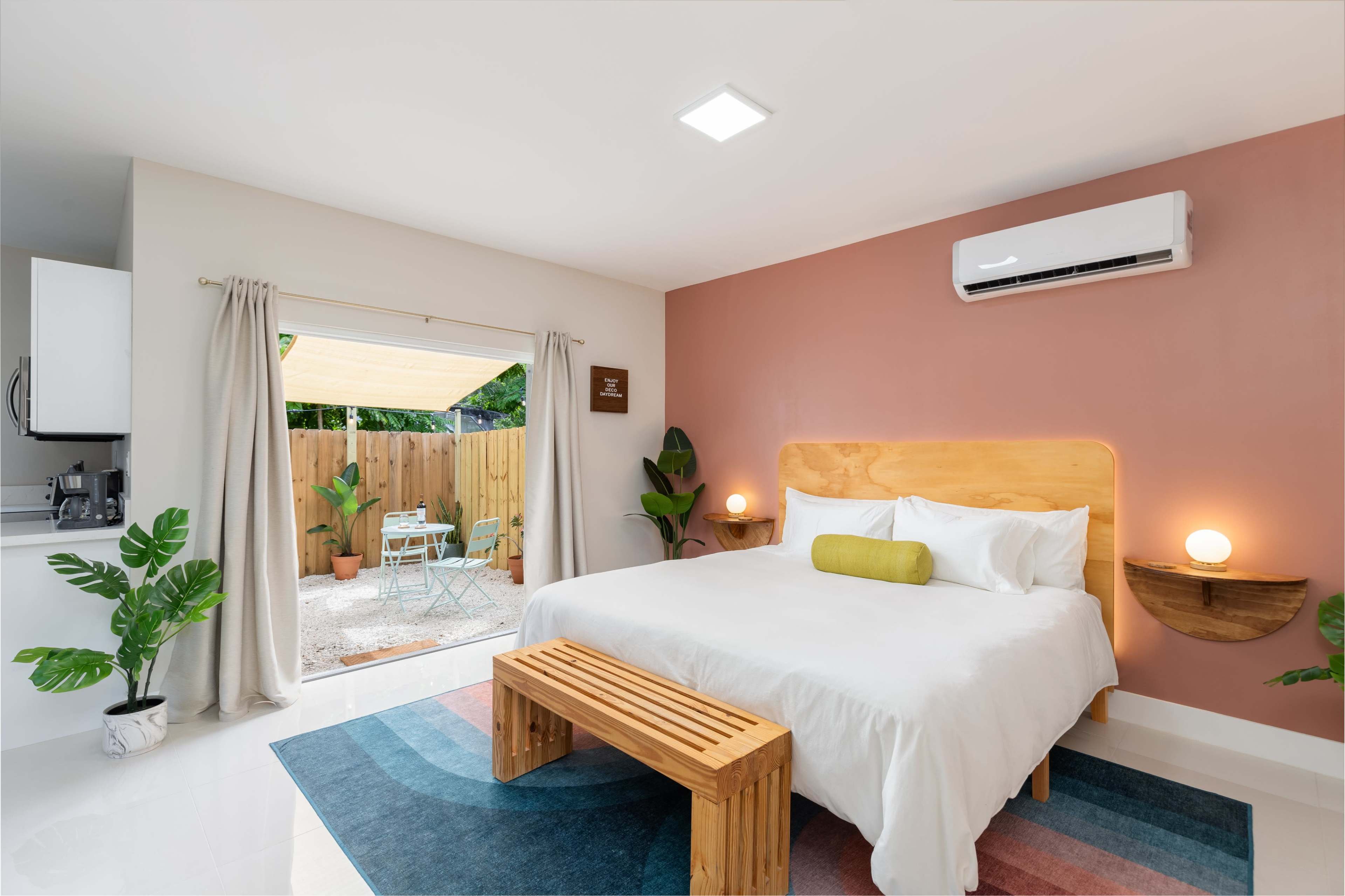 A spacious bedroom features a large bed, a wooden bench, and an open door leading to a patio area with outdoor seating.