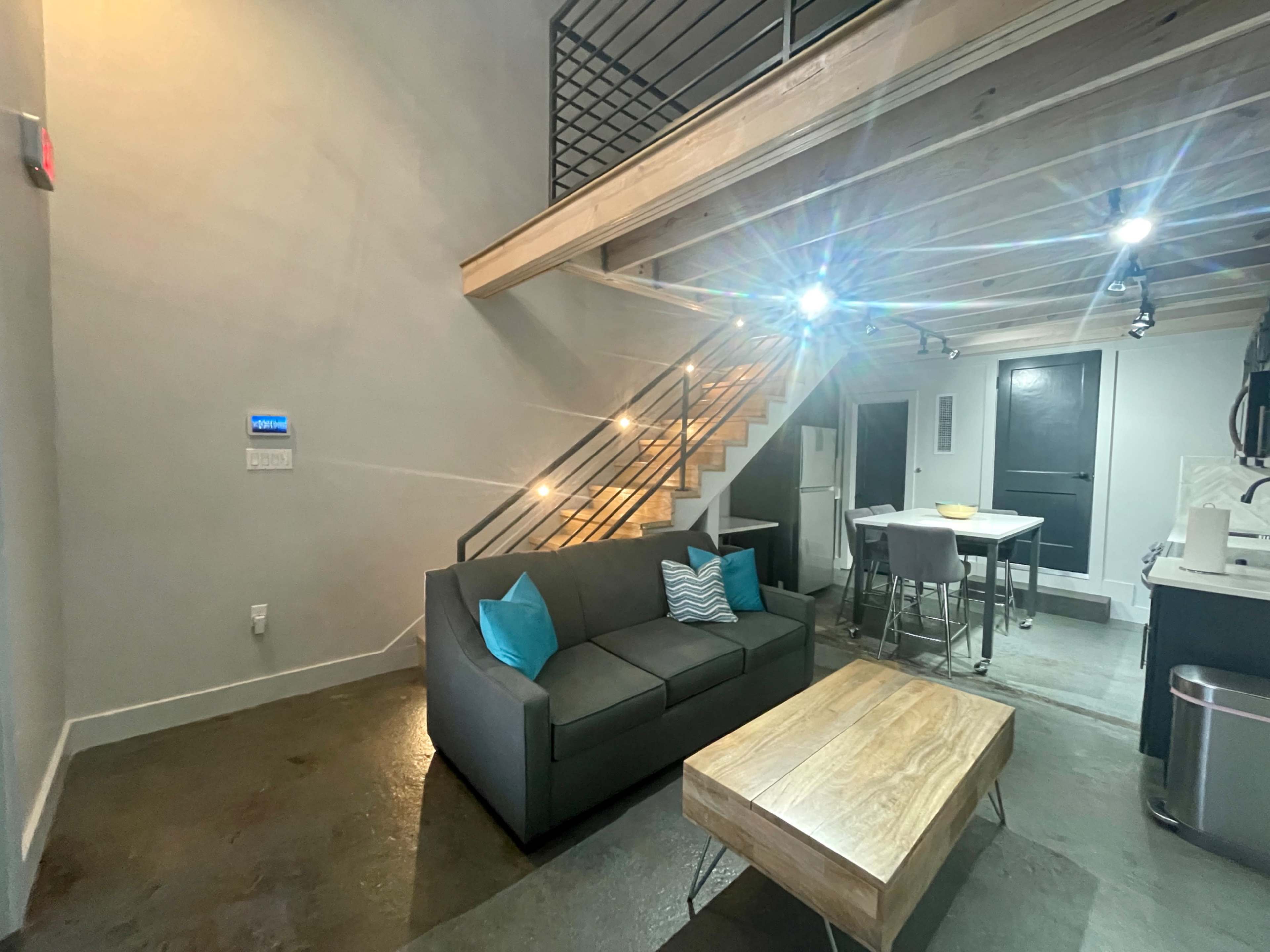 A modern living space with a gray sofa, a wooden coffee table, and a staircase leading to an upper level.
