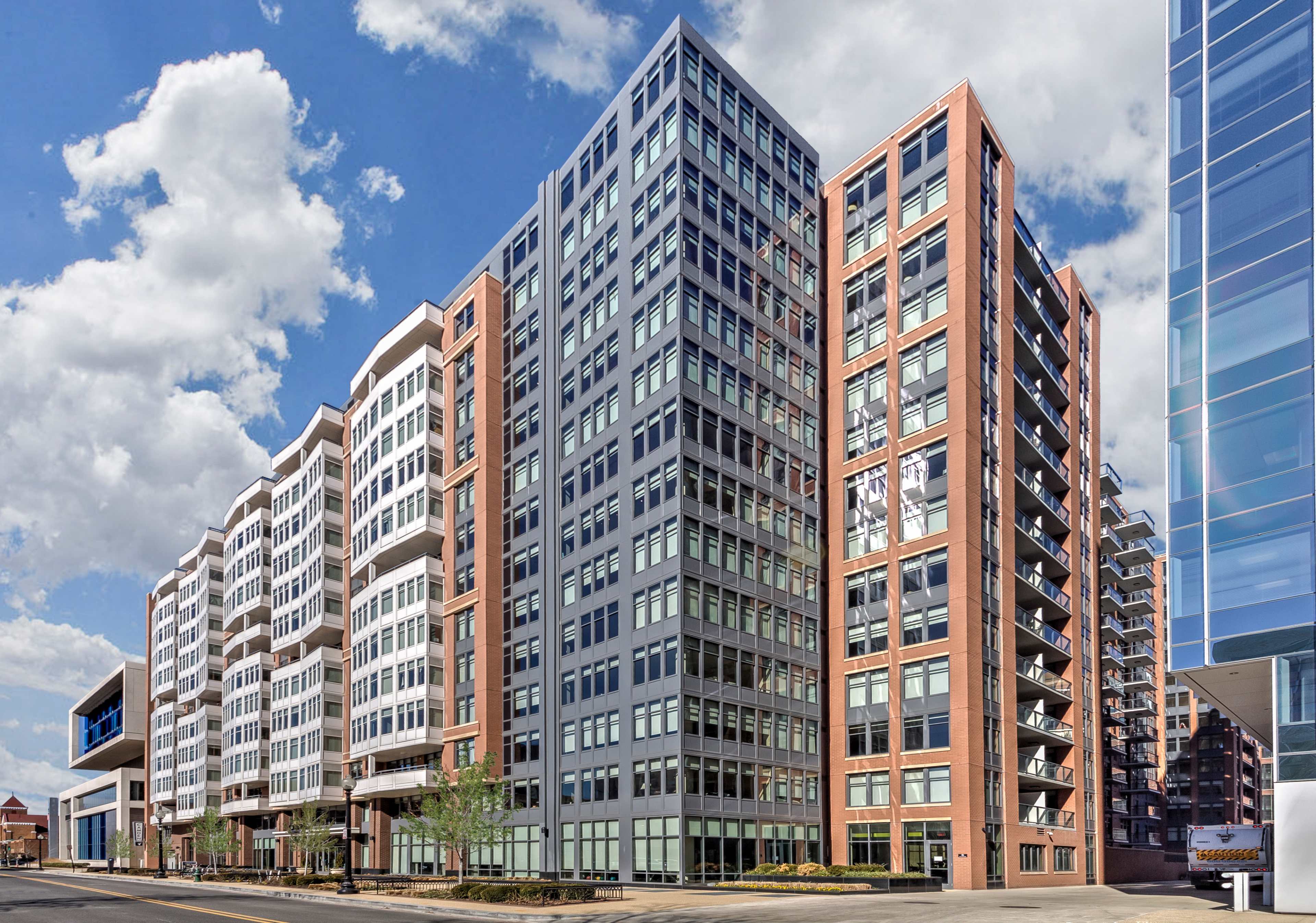 A modern residential building with a combination of brick and glass facades set against a partly cloudy sky.