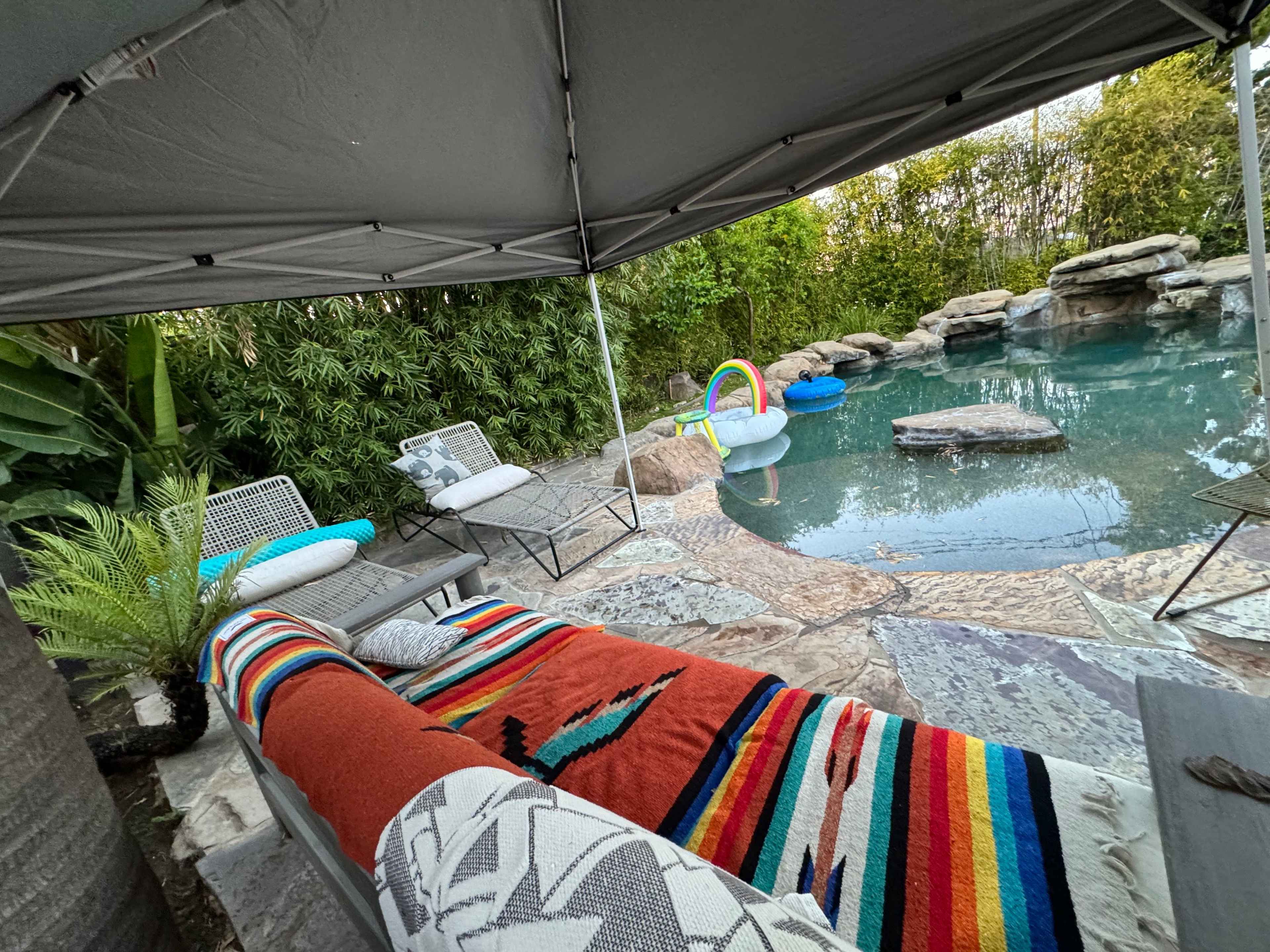 A shaded outdoor area features a pool surrounded by stone landscaping and lounge chairs.