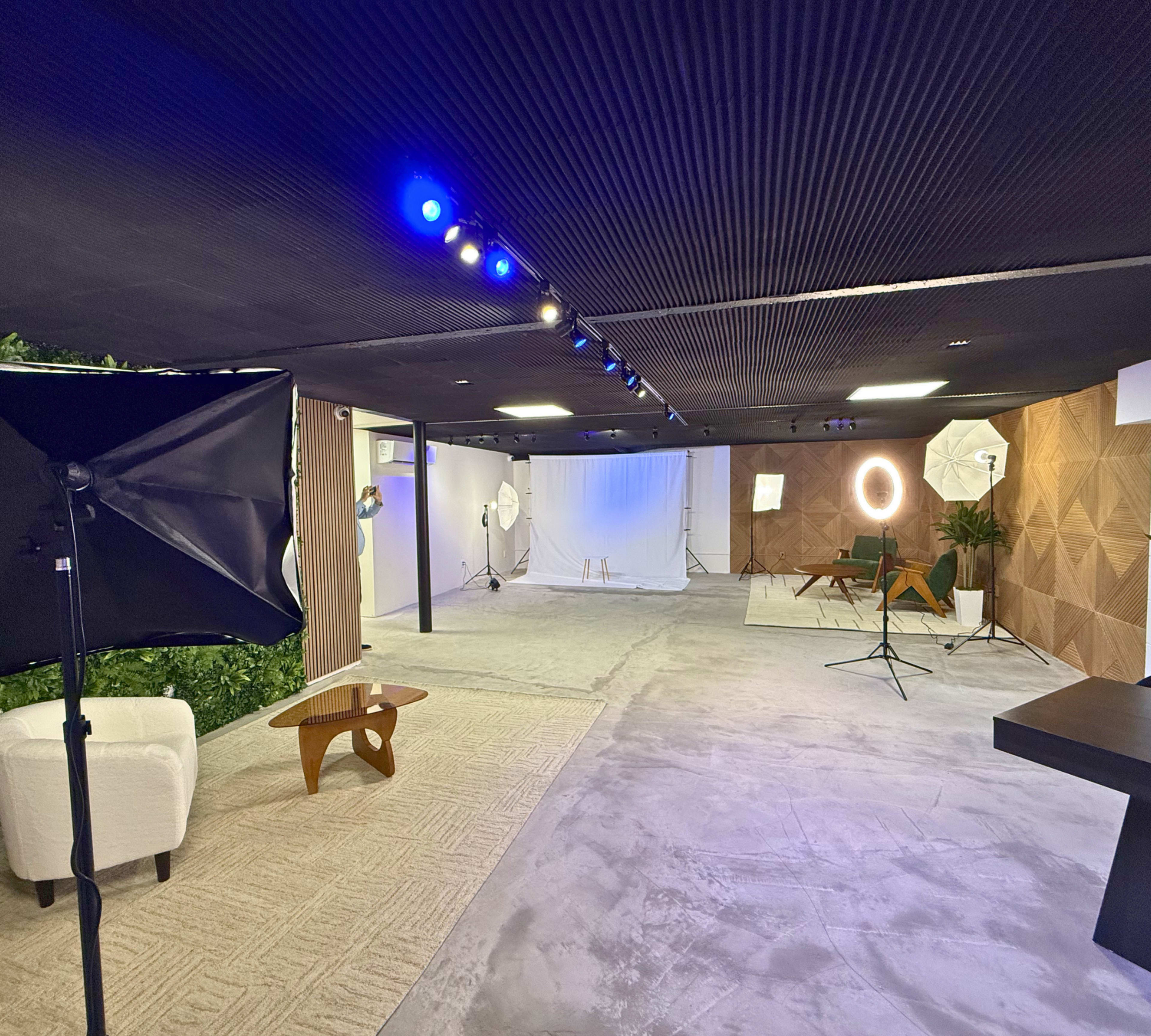 The image depicts a spacious photography studio with various lighting equipment, a backdrop, and a minimalistic setup including a chair and a table.