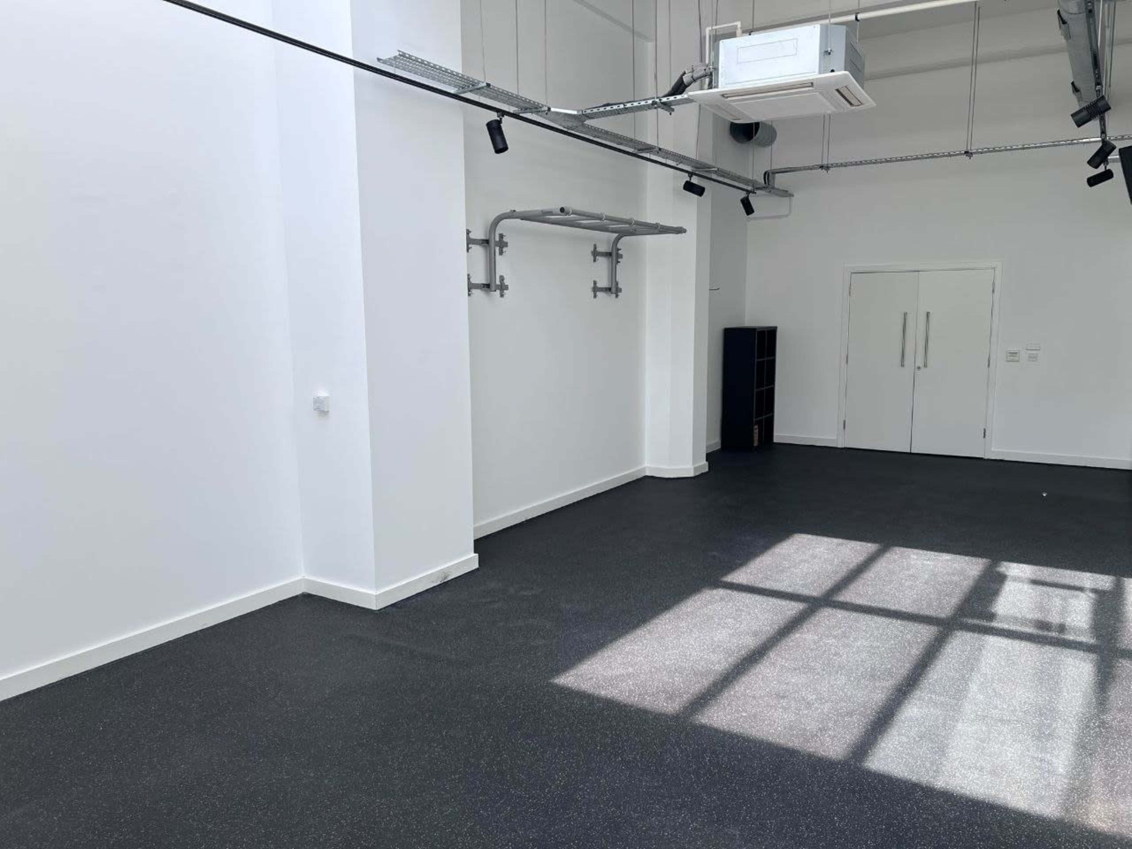 The image shows a spacious, empty room with white walls, a dark floor, and a large window casting shadows on the ground.
