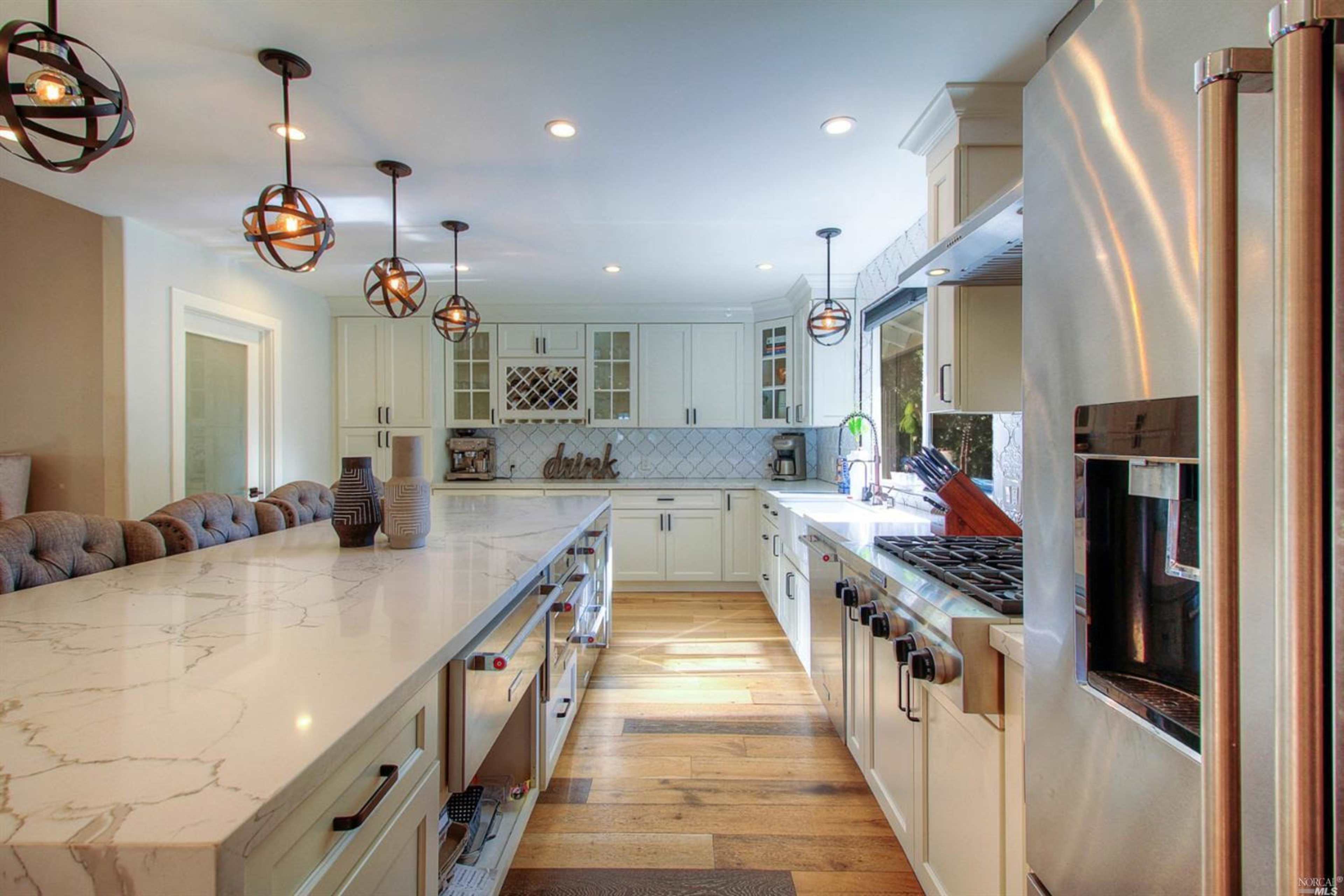 A spacious kitchen with white cabinetry, a large marble countertop, and modern appliances.
