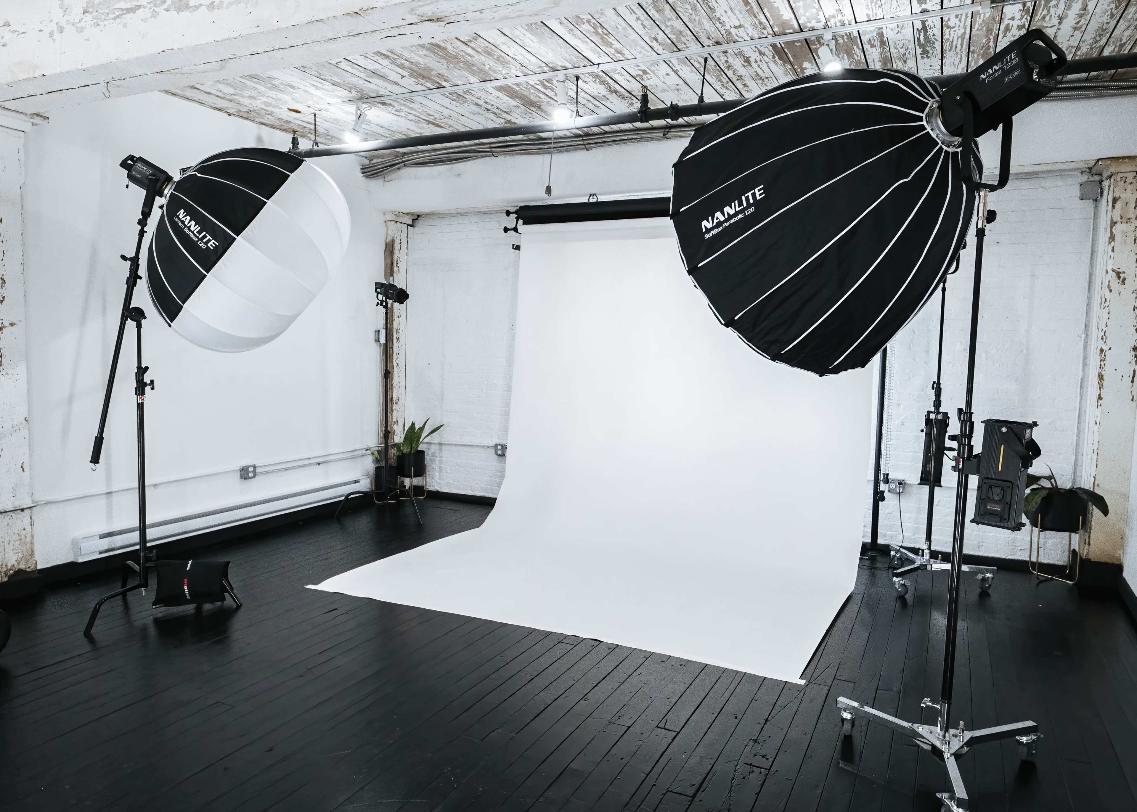 A photography studio equipped with two large softbox lights and a plain white backdrop on a wooden floor.