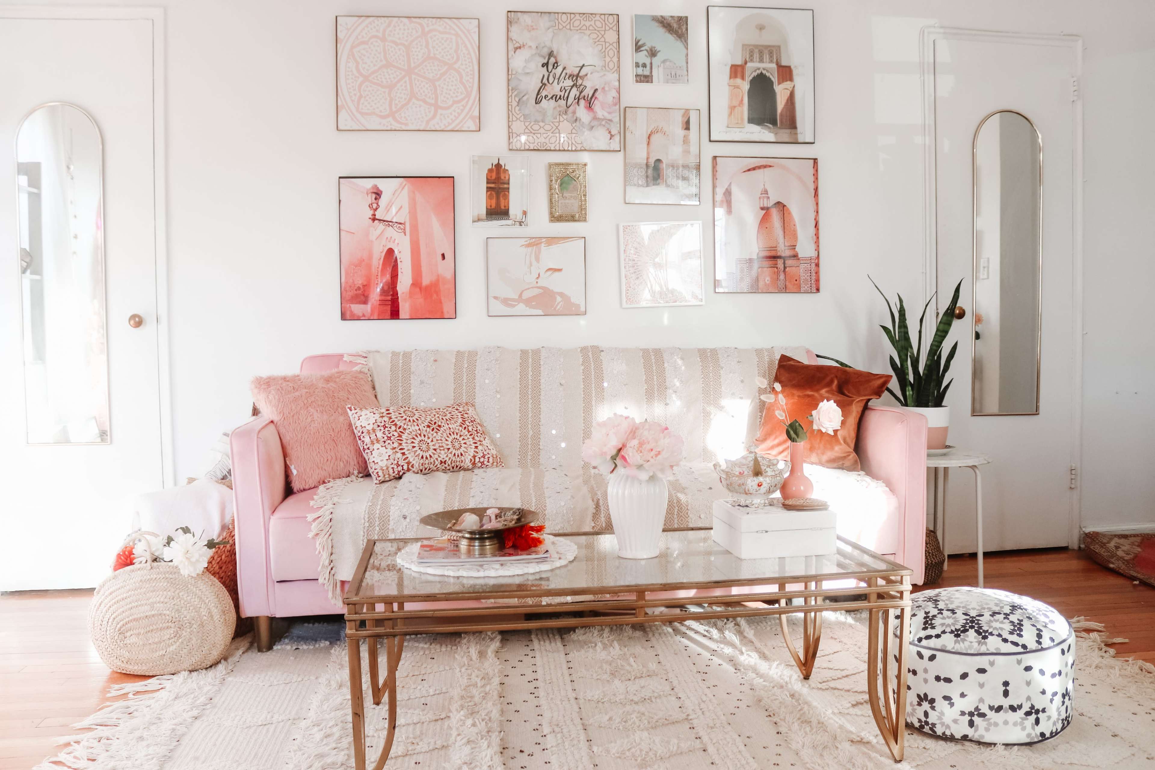 A well-decorated living room features a pink sofa with various decorative pillows, a glass coffee table, and artwork on the walls.