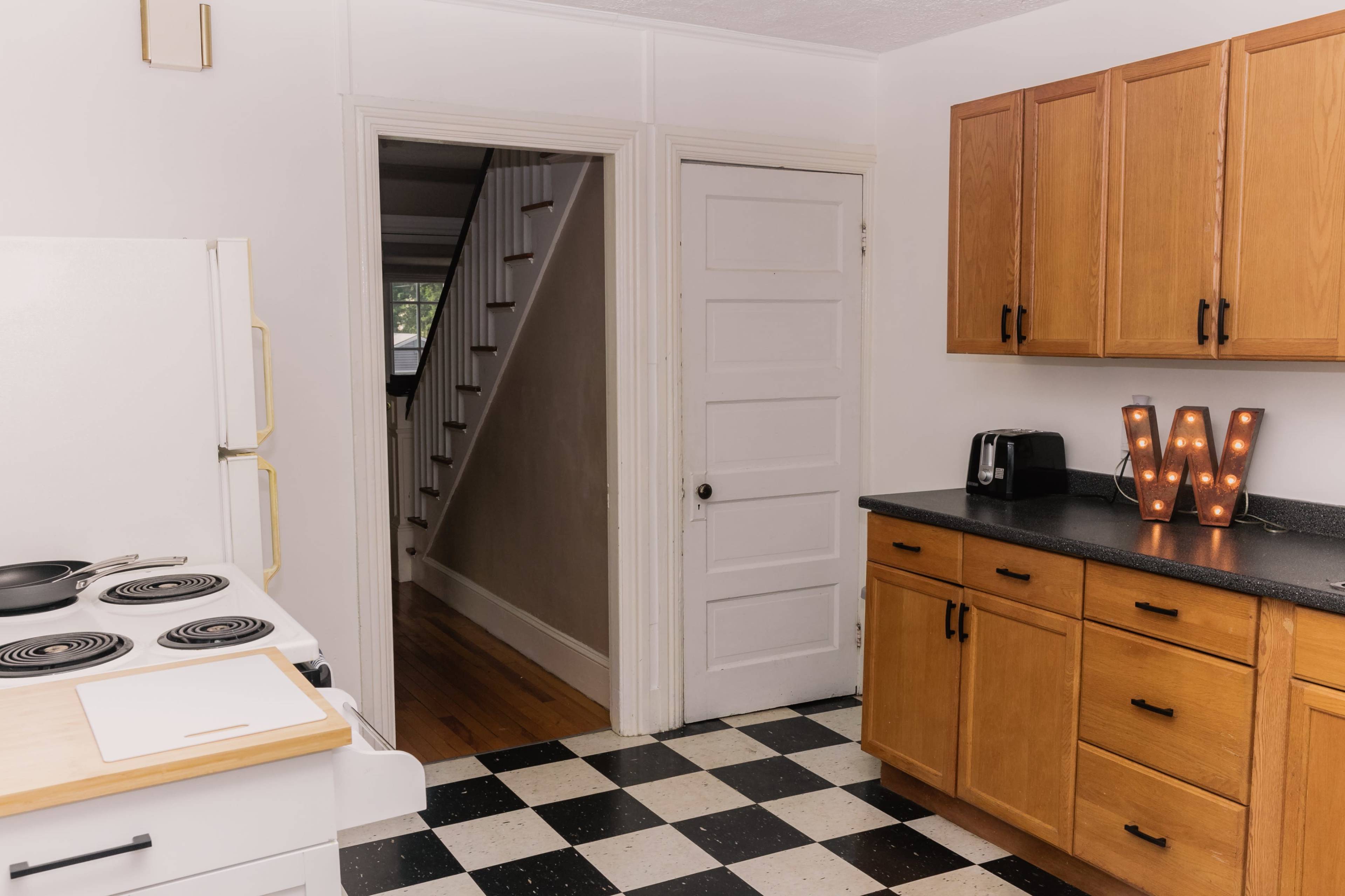 A kitchen with wooden cabinets, a white stove, and a doorway leading to a hallway with a staircase.
