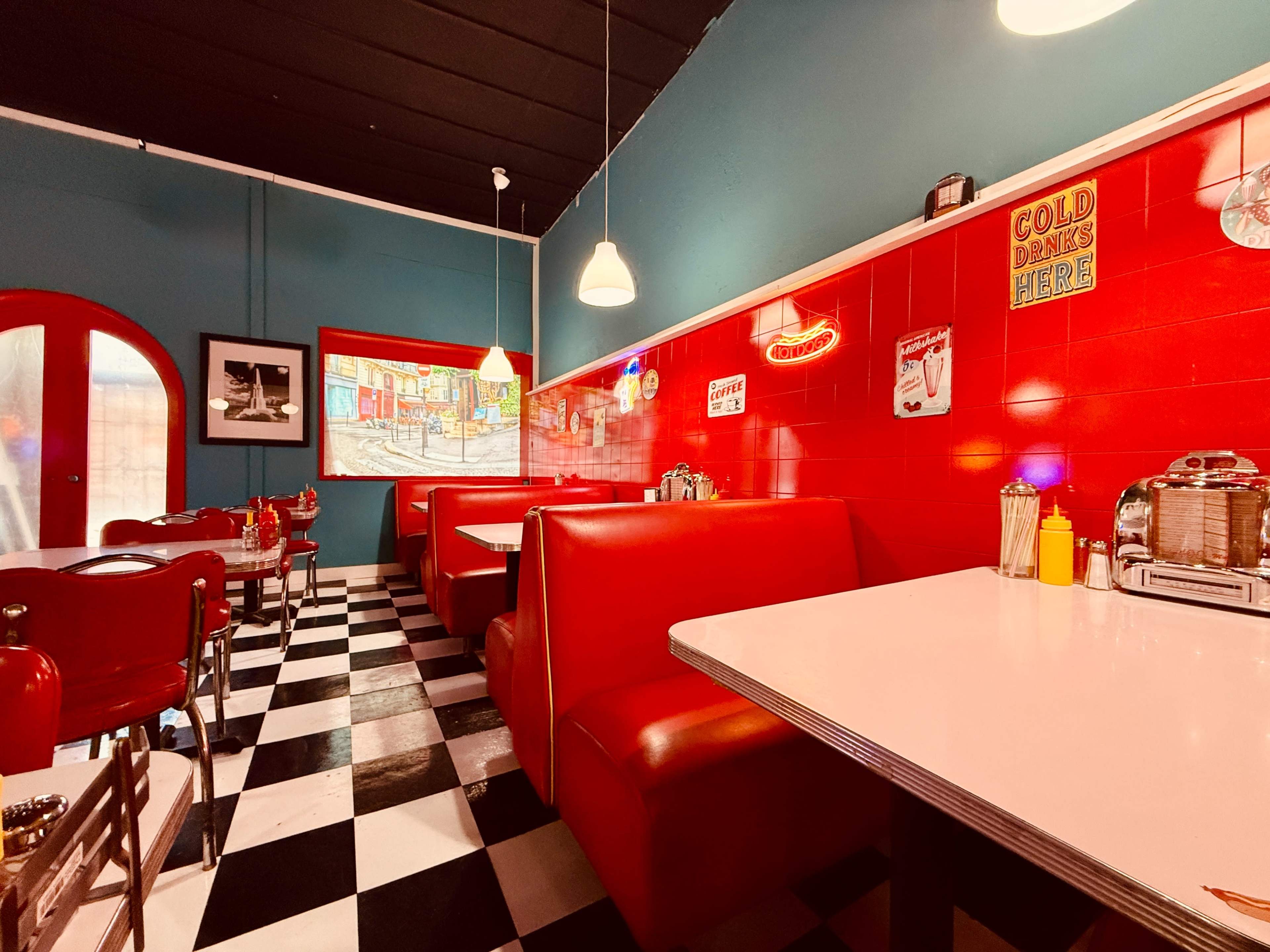 The image shows a retro-style diner interior featuring red booths, a checkered black-and-white floor, and vintage decor on the walls.