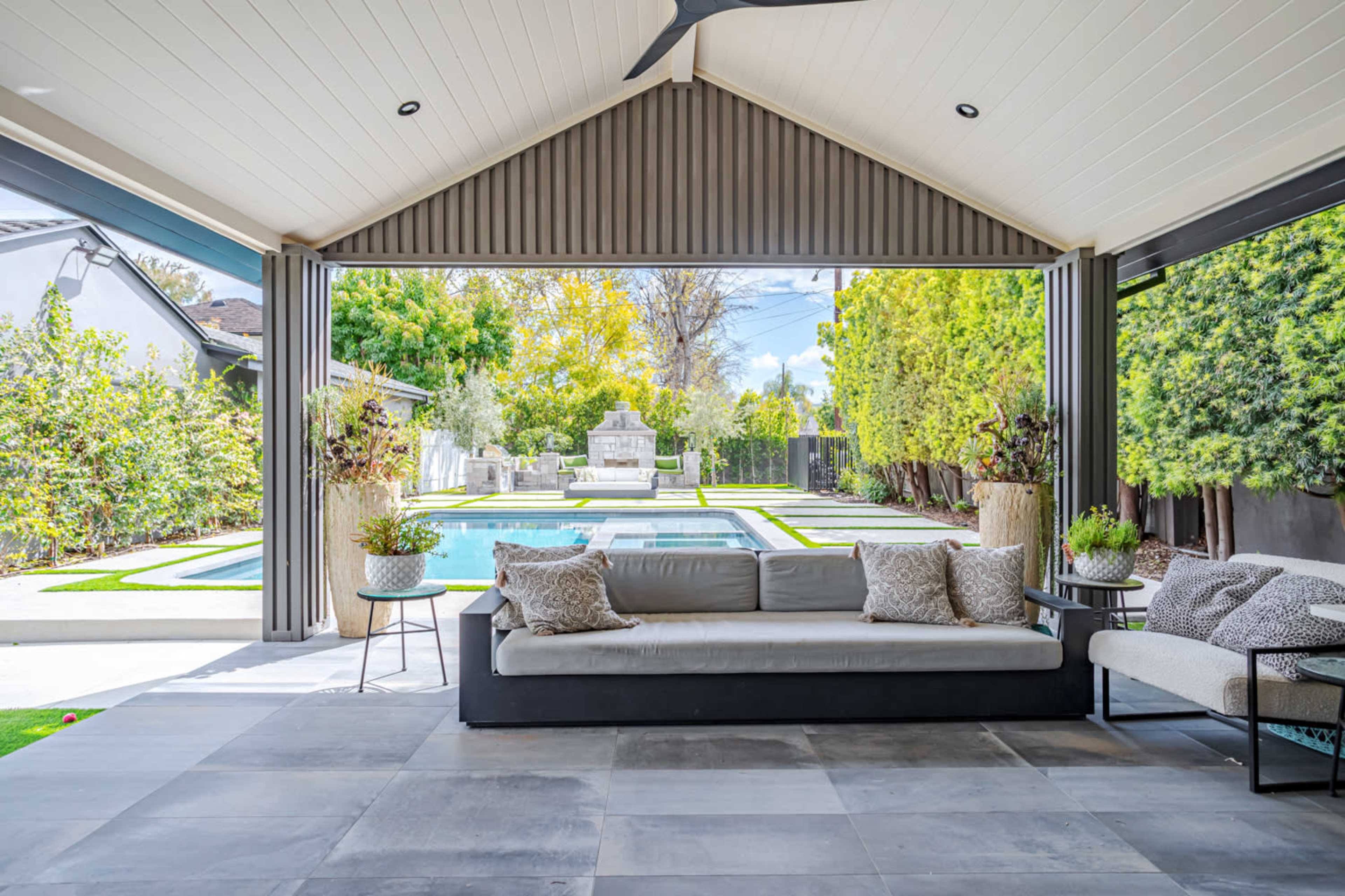A spacious outdoor living area features a comfortable sofa, overlooking a pool surrounded by greenery and decorative landscaping.