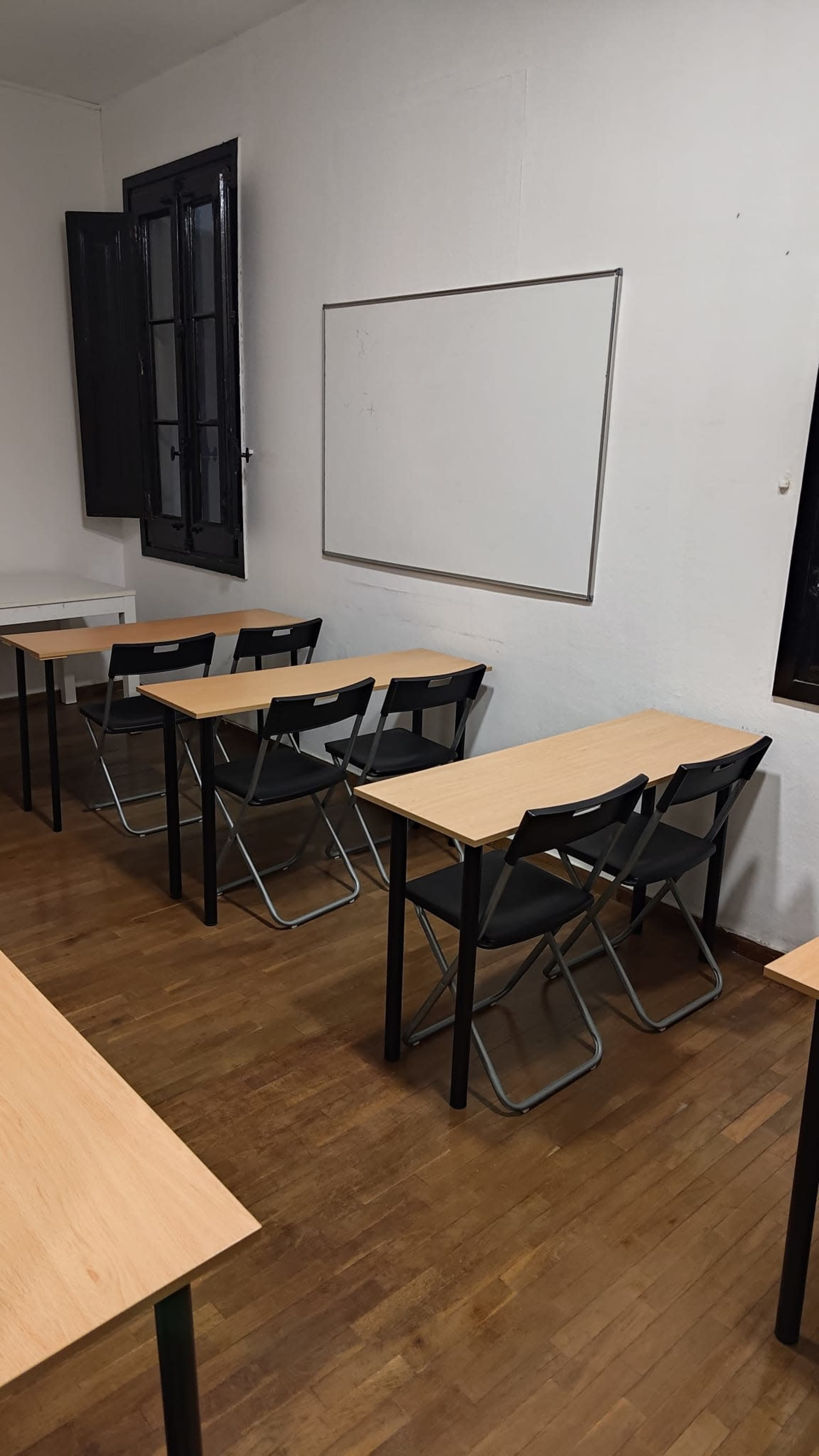 The image shows a classroom with several wooden desks arranged in rows and a whiteboard mounted on a wall.