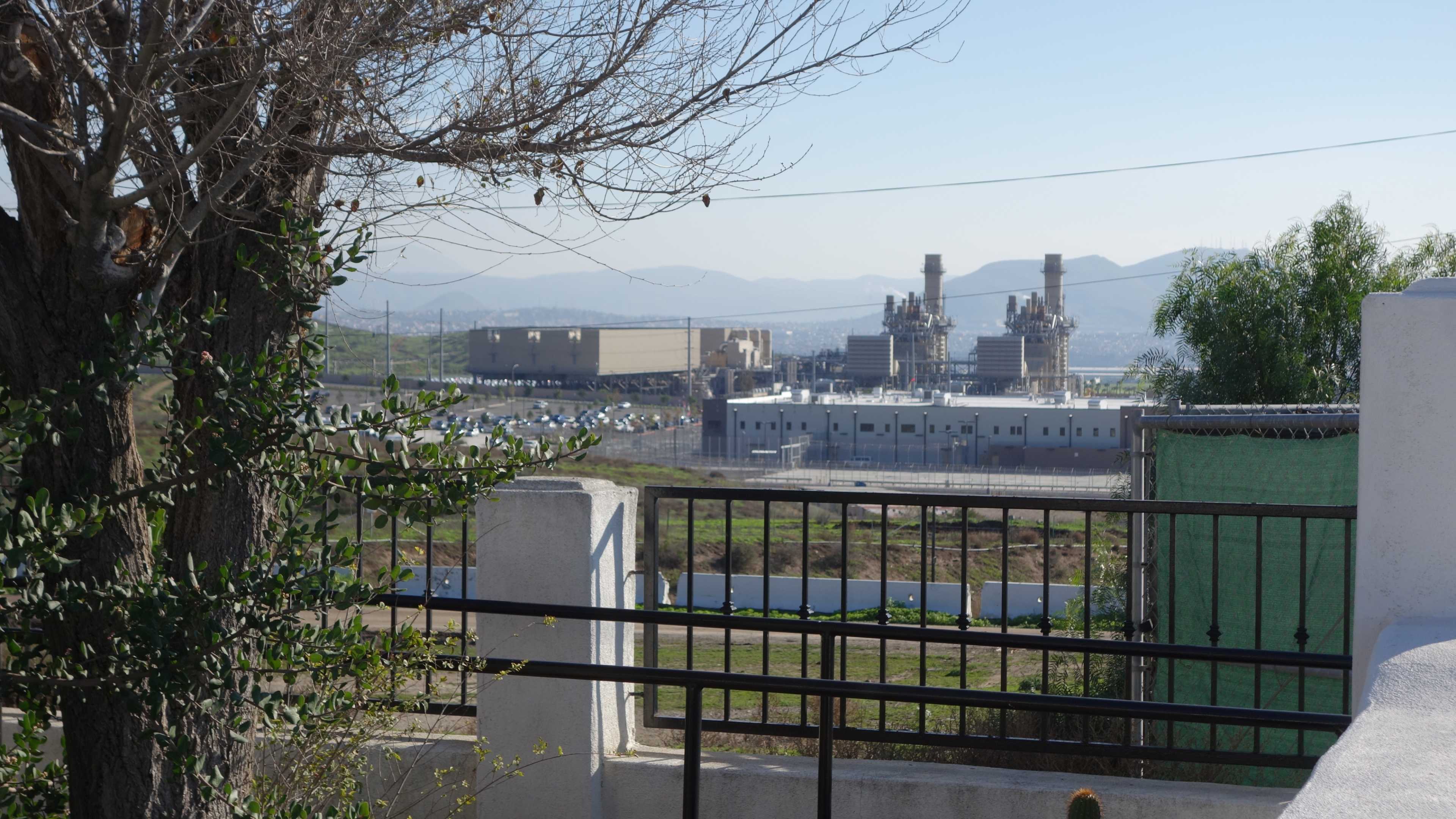 A landscape with a view of an industrial facility in the background, surrounded by hills and vegetation.