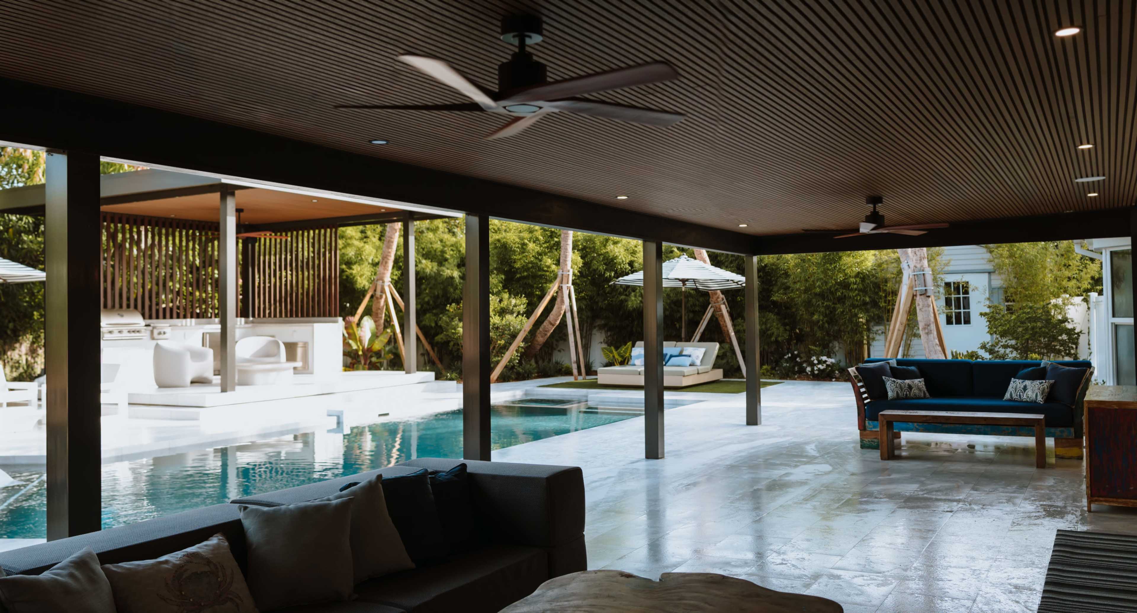 The image shows a modern outdoor living space with a pool, lounging area, and shaded seating surrounded by greenery.